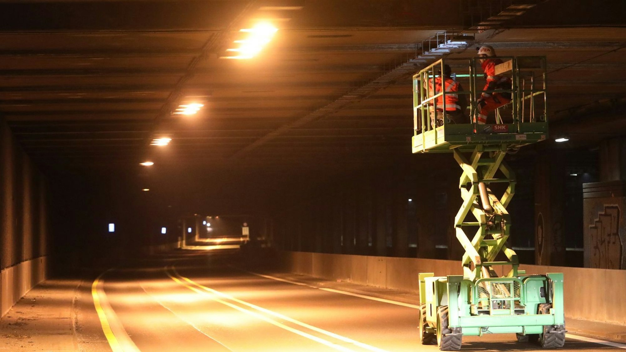 Auf einem ausgefahrenen Hubsteiger arbeiten Personen an der Decke des Tunnels Oberdollendorf, der gelb beleuchtet und für den Verkehr gesperrt ist.