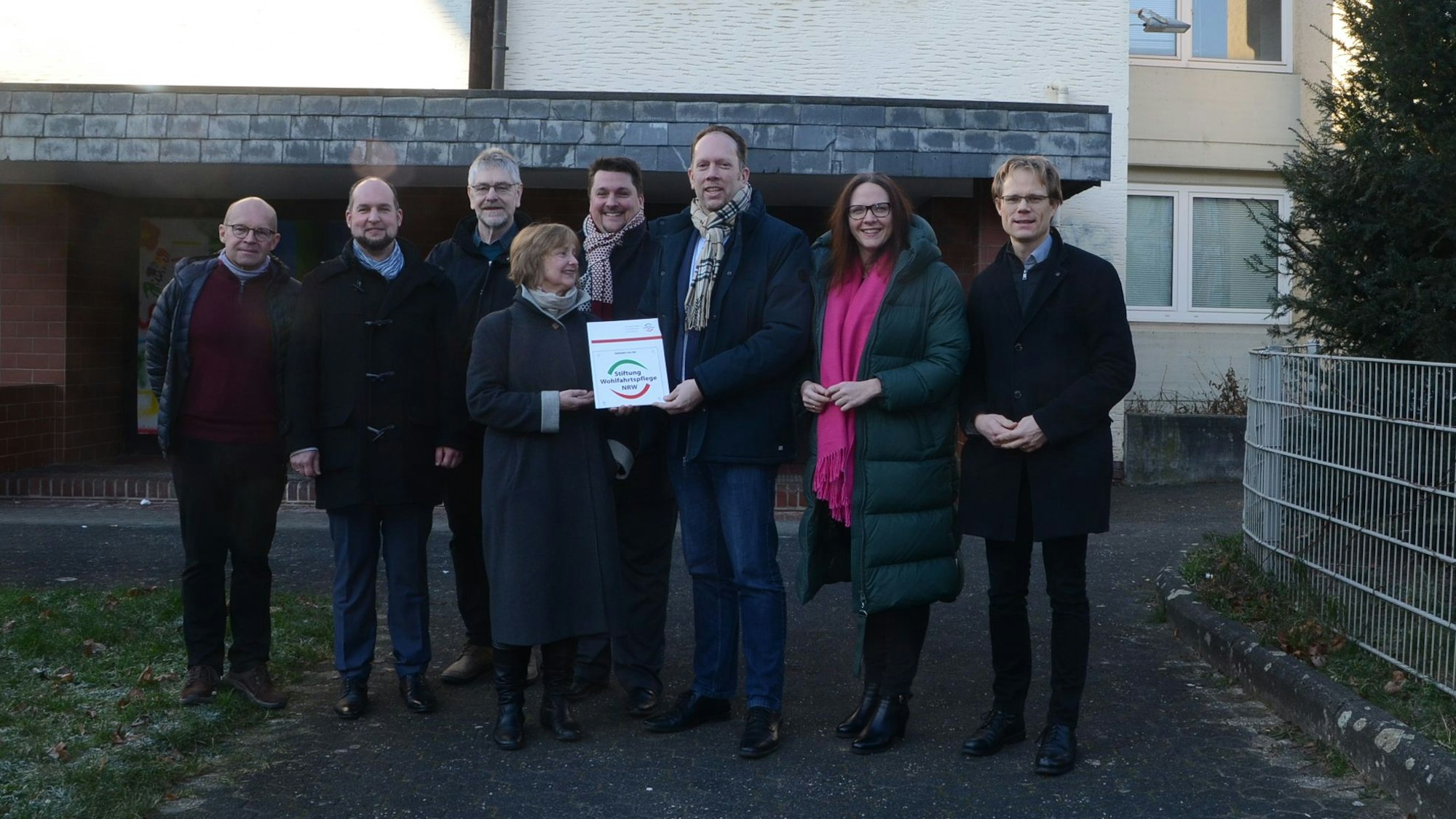 Männer und Frauen stehen vor einem Gebäude aus den 1970er Jahren.