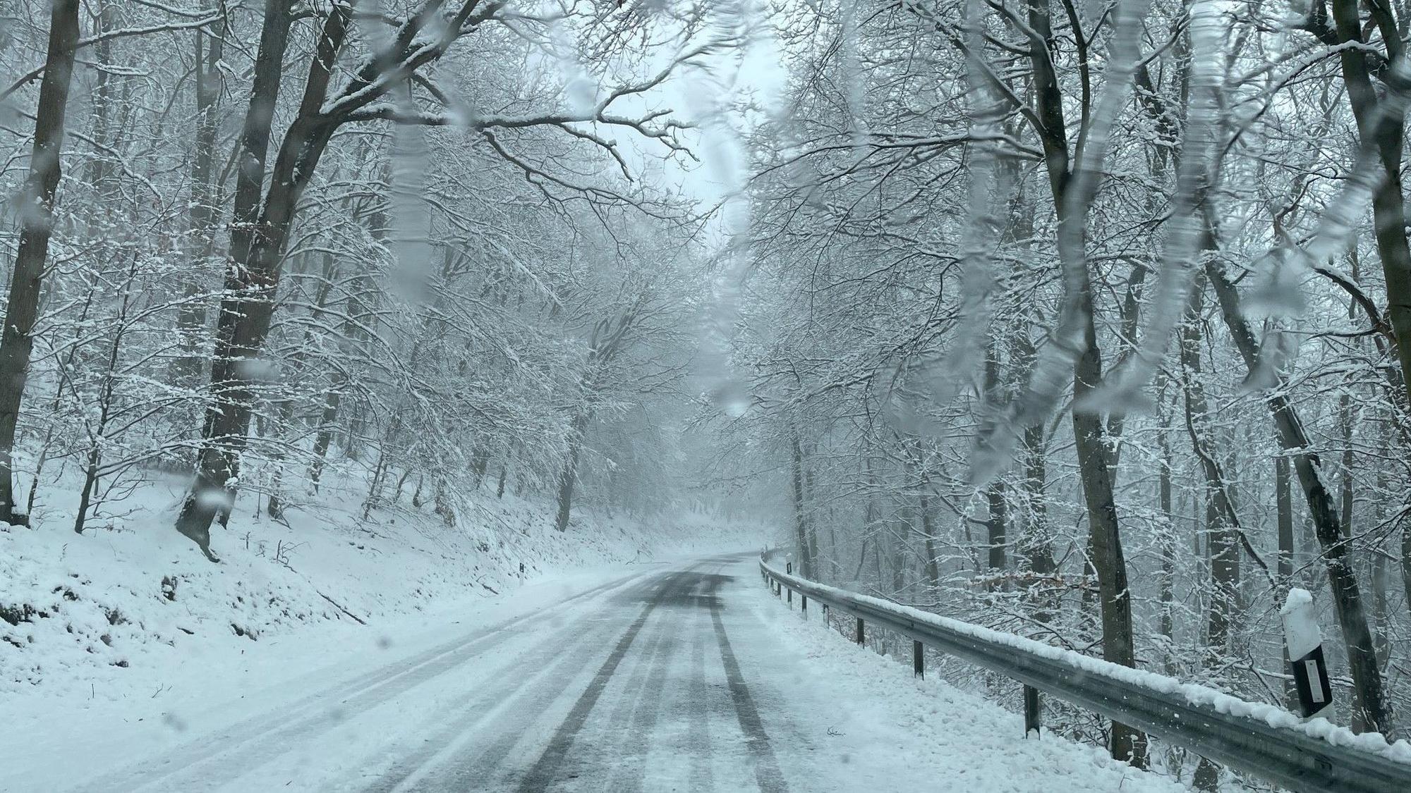 Eine eingeschneite Straße in der Eifel ist verlassen. Links und rechts der Fahrbahn liegen Schneemassen. (Archivbild)