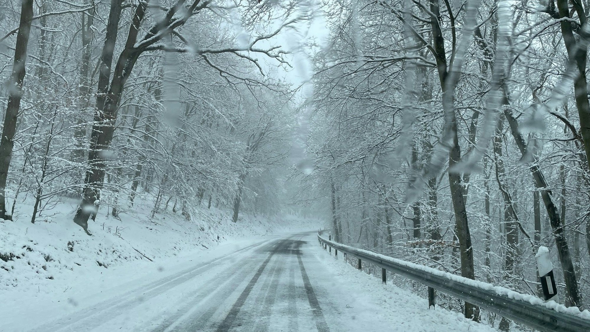 Eine eingeschneite Straße in der Eifel ist verlassen. Links und rechts der Fahrbahn liegen Schneemassen. (Archivbild)