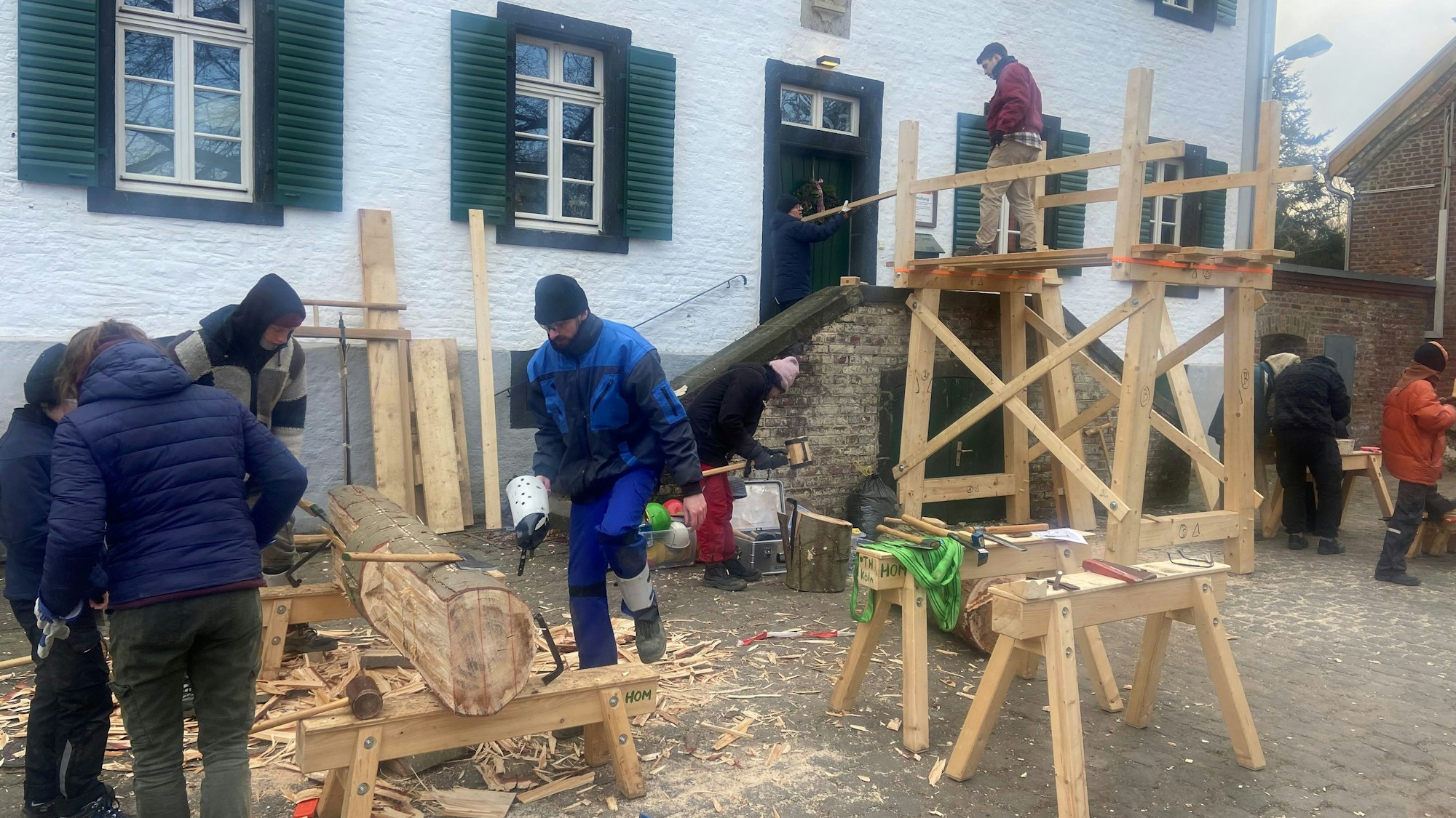 Vor einem Fachwerkgebäude mit grünen Fensterläden sind Holzarbeiten im Gange.