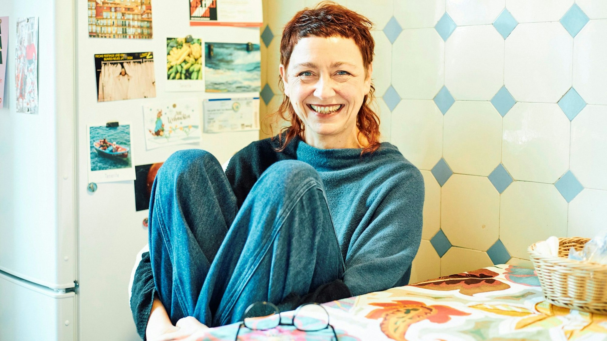 Barbara Fuchs sitzt mit angewinkelten Beinen an einem Küchentisch.