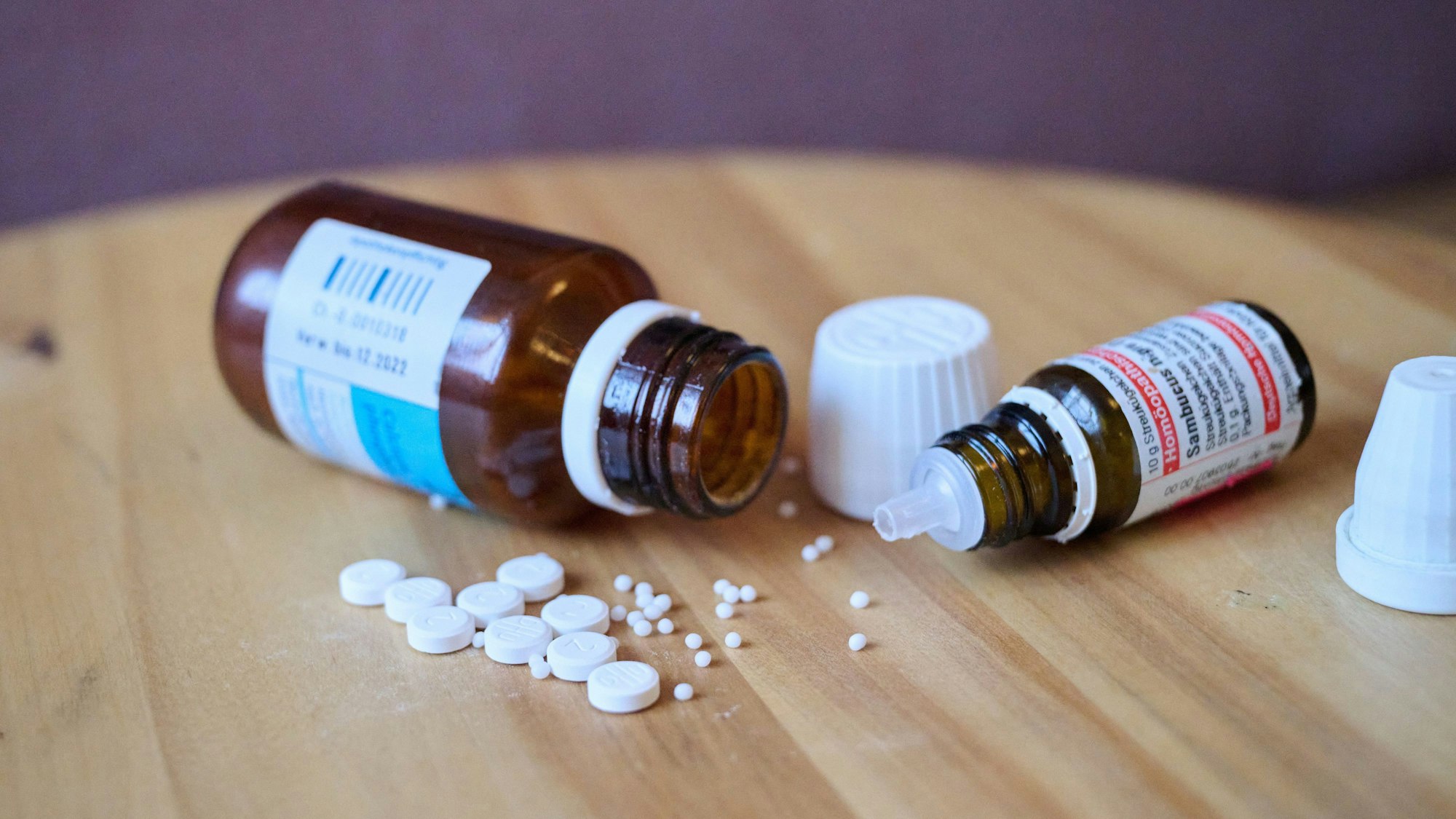 Homöopathische Glasfläschchen, Kügelchen und Tabletten liegen auf einem Tisch.