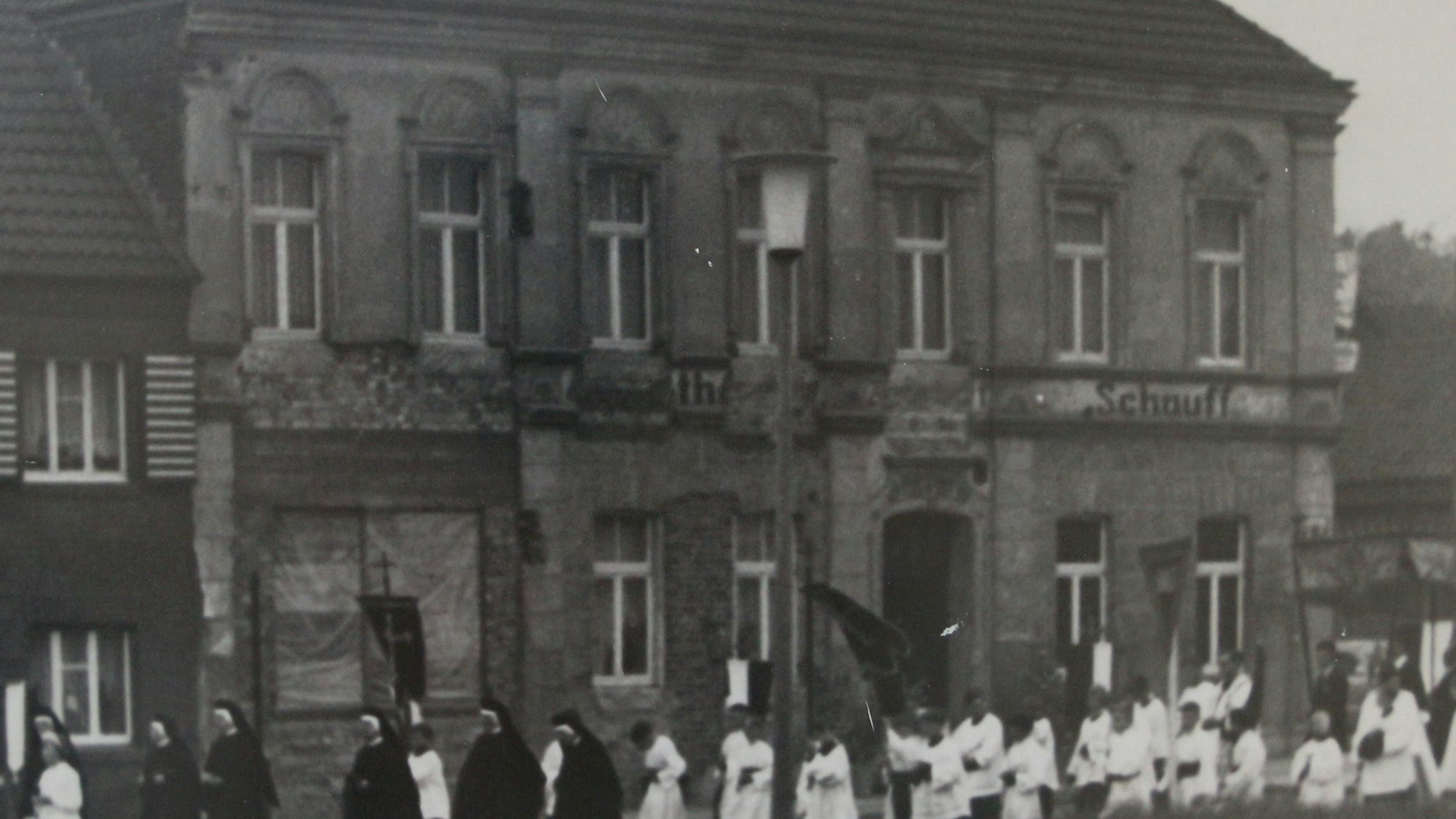 Das Foto zeigt eine Außenaufnahme von Haus Schauff aus dem Jahr 1962. Eine Prozession zieht vorbei.