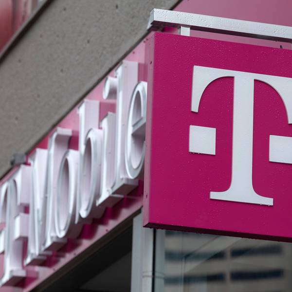 Ein Logo der Deutschen Telekom bzw. T-Mobile ist vor einem Geschäft in einer Innenstadt zu sehen.