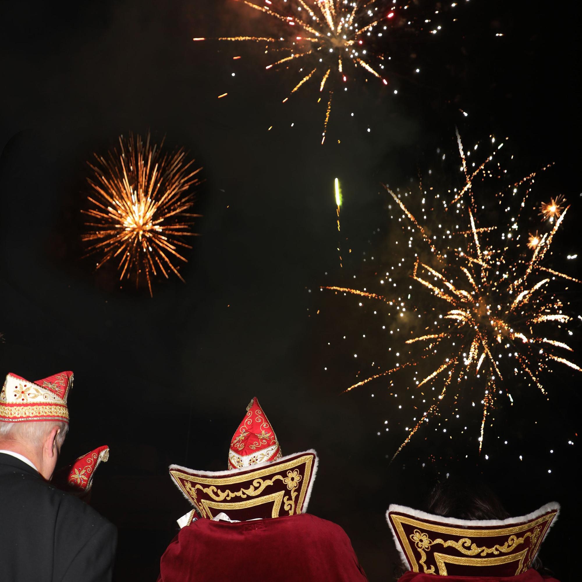 Das angehende Dreigestirn schaut zum Himmel, wo ein Feuerwerk zu sehen ist.