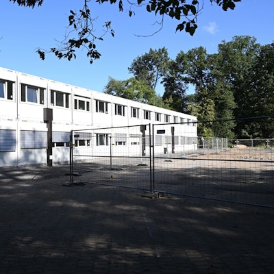 Ein großer Containerbau hinter Bauzäunen.