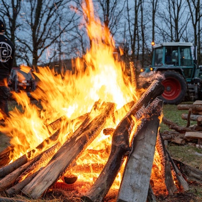 05.01.2024, Bayern, Burgpreppach: Ein Schlepper fährt an einem Feuer vorbei. An der Bundesstraße 303 in Burgpeppach sowie rund 14 weiteren Orten in Franken demonstrieren Landwirte am Freitagabend mit Mahnfeuern unter dem Motto "Franken in Flammen" gegen geplante Kürzungen der Agrardiesel-Subventionen und die Abschaffung von Kfz-Steuererleichterungen in der Land- und Forstwirtschaft. Foto: Pia Bayer/dpa +++ dpa-Bildfunk +++