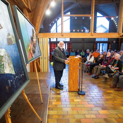 Künstler Uwe Appold hält einen Vortrag. Hinter ihm stehen mehreren Bilder.