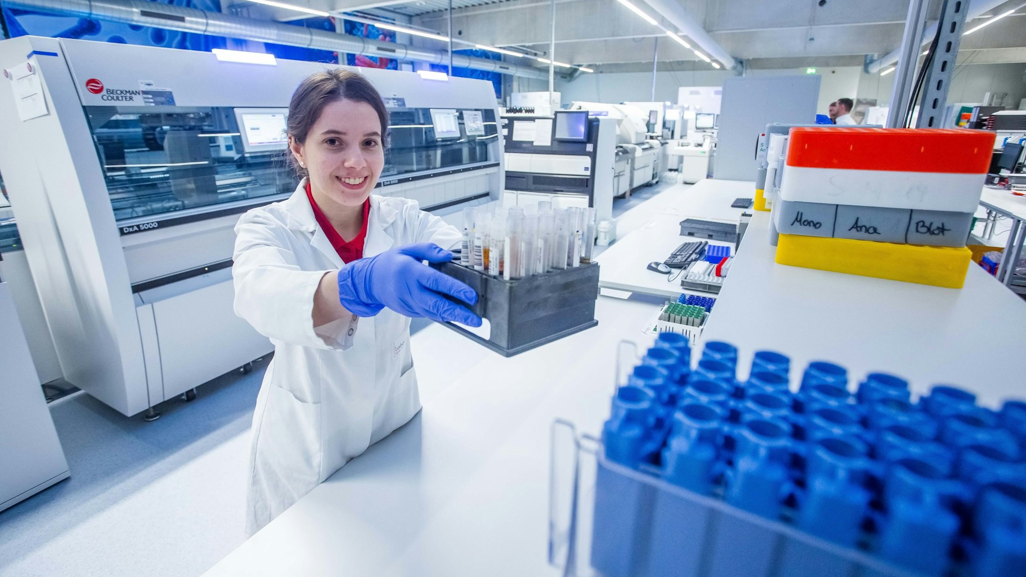 Eine Frau mit Kittel hält in einem Labor eine Kiste mit Probenröhrechen in der Hand.