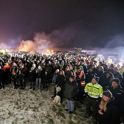 Zahlreiche Menschen stehen auf einem Feld zusammen. An einem Traktor im Hintergrund waren Deutschland-Fahnen kopfüber angebracht. Der Landwirt erhielt eine Ordnungswidrigkeiten-Anzeige der Polizei, weil die Flaggen den Bundesadler zeigten und dieses Hoheitszeichen amtlichen Stellen des Bundes vorbehalten ist.