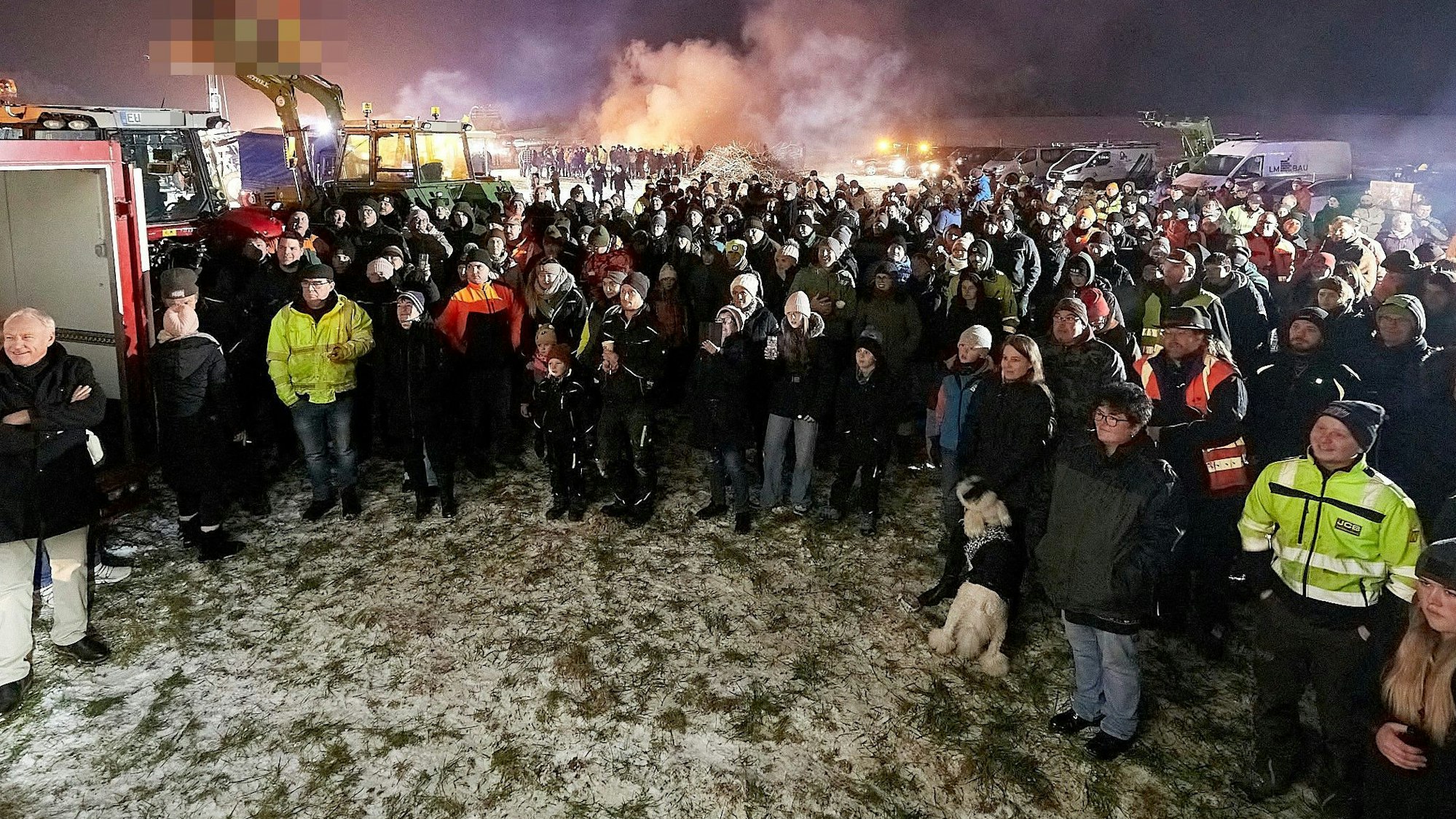 Zahlreiche Menschen stehen auf einem Feld zusammen. An einem Traktor im Hintergrund waren Deutschland-Fahnen kopfüber angebracht. Der Landwirt erhielt eine Ordnungswidrigkeiten-Anzeige der Polizei, weil die Flaggen den Bundesadler zeigten und dieses Hoheitszeichen amtlichen Stellen des Bundes vorbehalten ist.