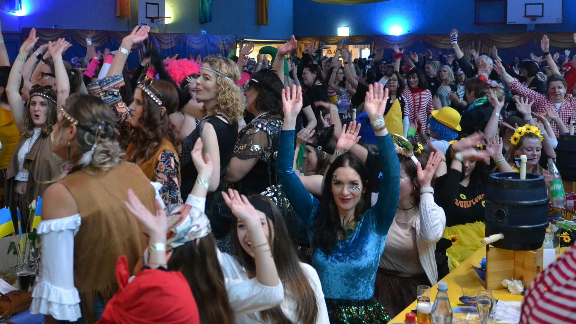 Bunt kostümierte Frauen, manche sitzend, die meisten stehend, recken gut gelaunt ihre Arme in die Höhe. Auf einem der Tische steht ein Bierfass.