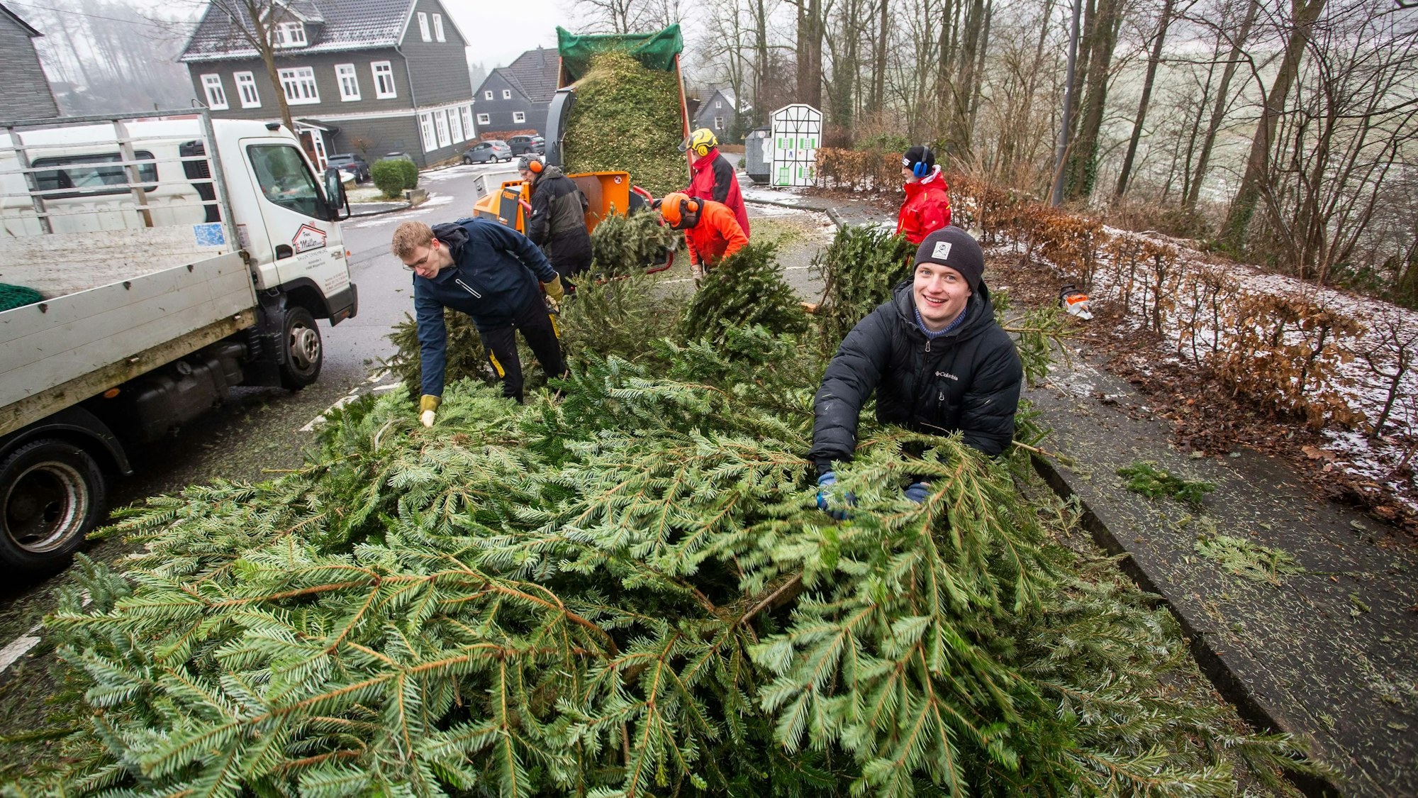 Freiwillige Helfer stapeln ausgediente Weihnachtsbäume an einem Straßenrand.