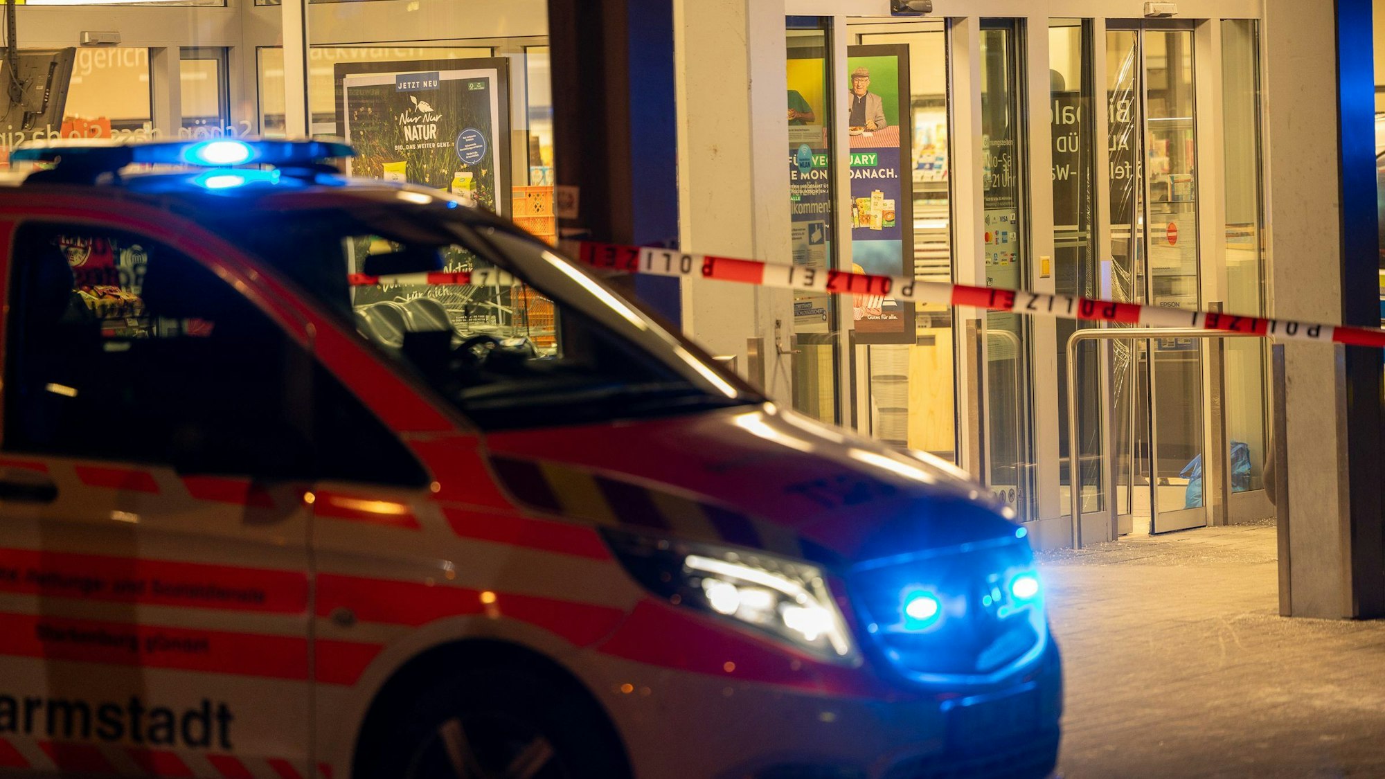 Ein Einsatzfahrzeug steht vor einem Supermarkt mit Blaulicht.