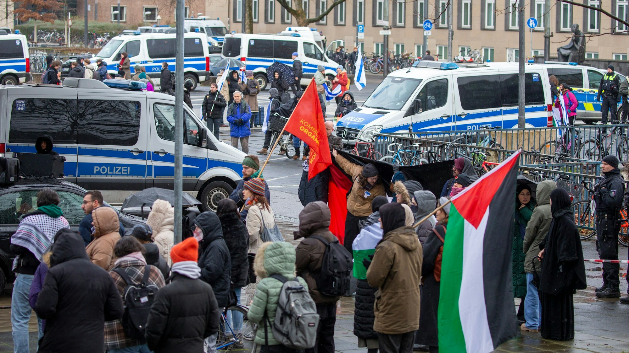 Palästinische und israelische Flaggen sowie Polizeiautos vor der Kölner Uni.