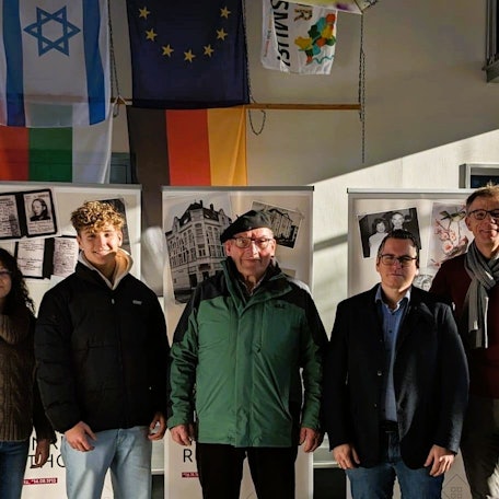 Bei der Eröffnung stehen Schüler, Lehrer und Bürgermeister Sascha Solbach vor den Ausstellungswänden.