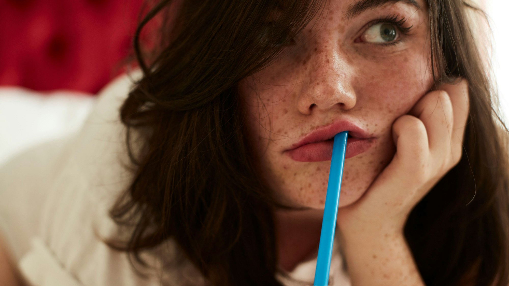 gelangweiltes Mädchen liegt mit Strohhalm im Mund auf dem Bett