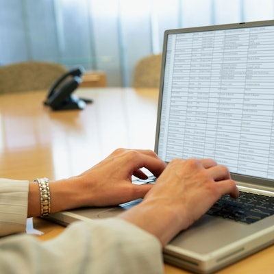 Zwei Hände tippen auf einem Laptop, auf dem Bildschirm ist eine Tabelle zu sehen.