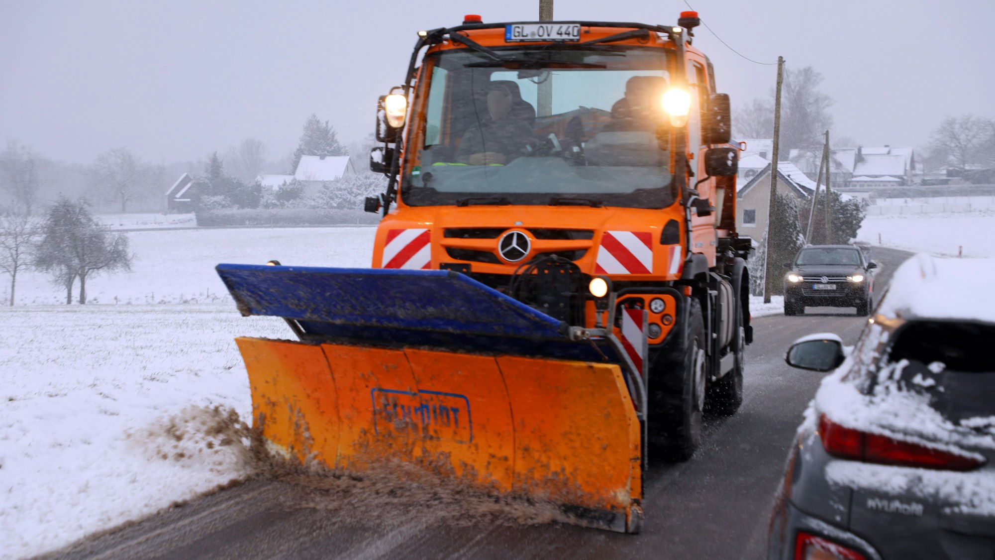 Ein Schneeräumfahrzeug auf einer mit Schneematsch bedeckten Straße ist zu sehen.