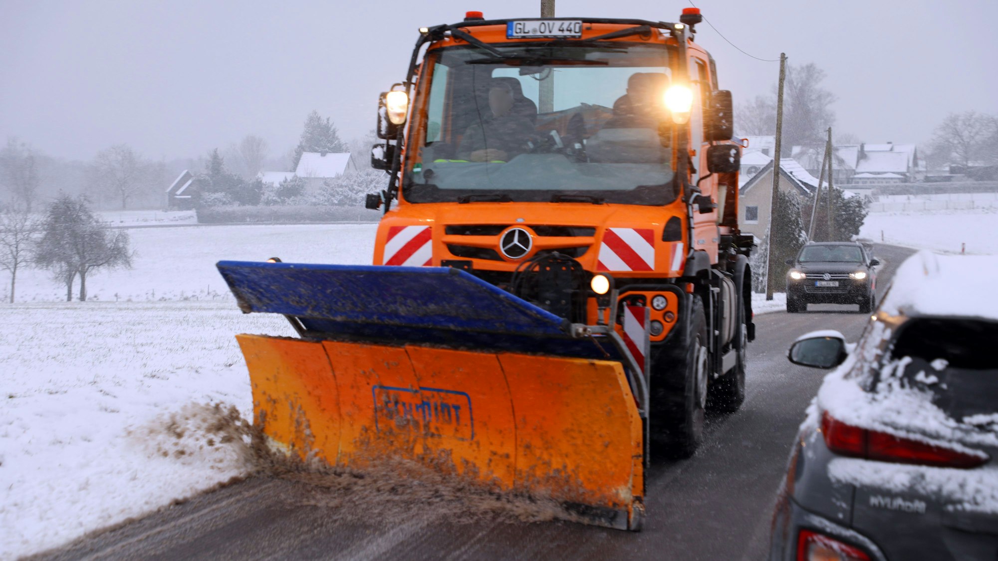 Ein Schneeräumer fährt auf einer winterlichen Straße und räumt Schneematsch von der Fahrbahn.