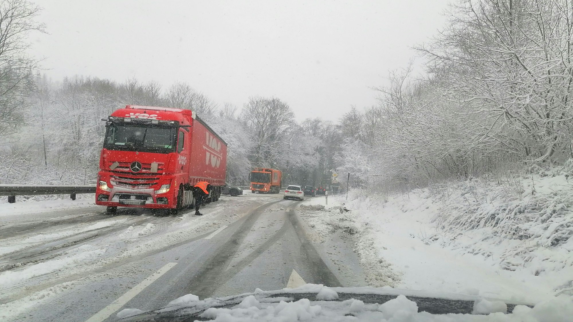 Ein roter Lkw hält auf dem Seitenstreifen einer Schnee-verwehten Straße.