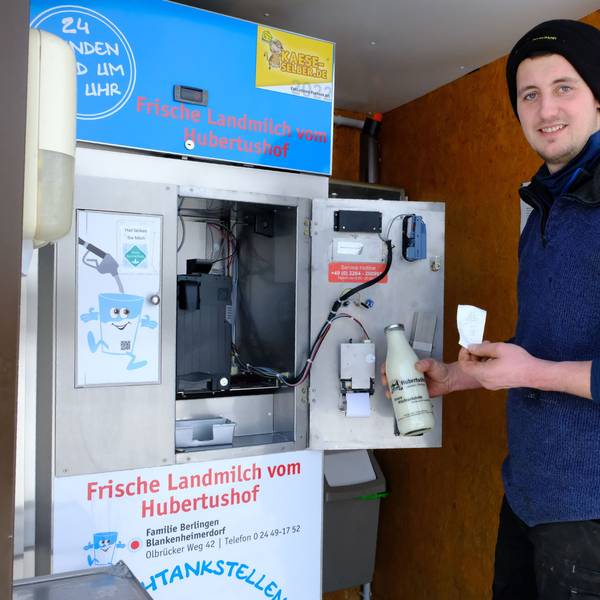 Rainer Berlingen steht mit einer Flasche Milch und einem Kassenbon in der Hand an der „Milchtankstelle“ auf seinem Hof.