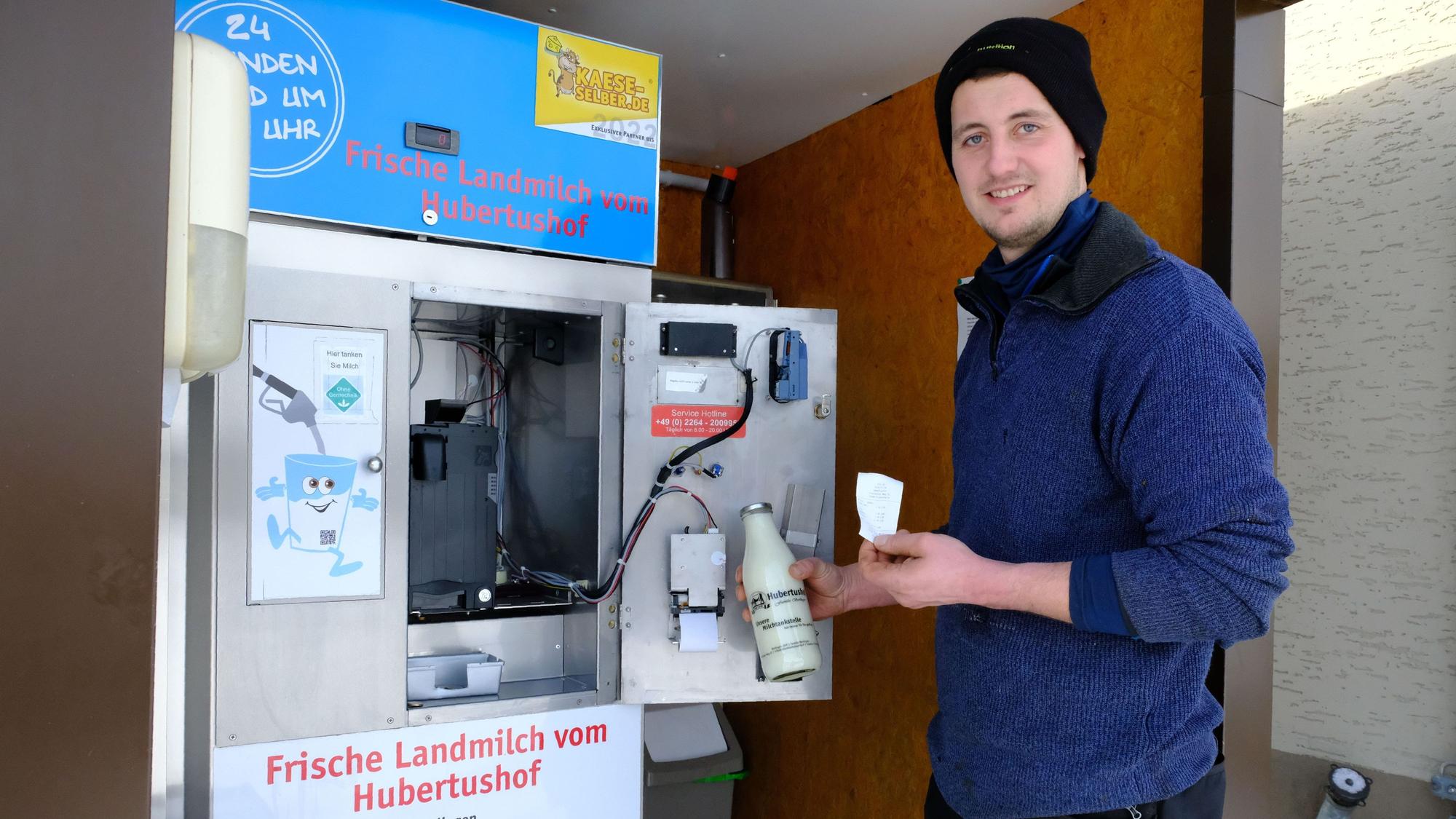 Rainer Berlingen steht mit einer Flasche Milch und einem Kassenbon in der Hand an der „Milchtankstelle“ auf seinem Hof.