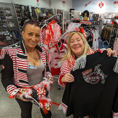Zwei kostümierte Frauen zeigen Hut und Jacke im Karnevalsladen im Hürth-Park.