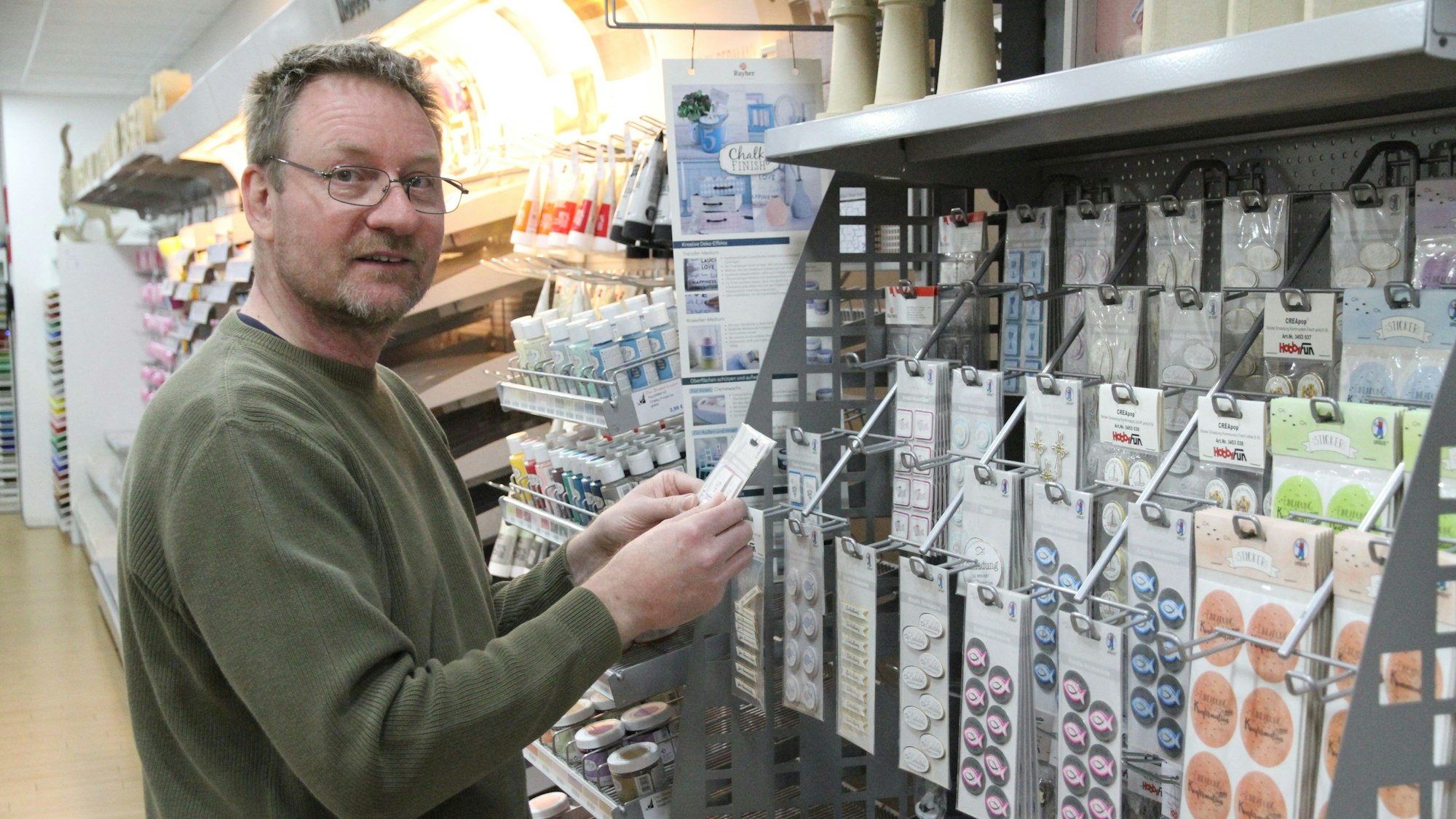 Ein Mann vor einem Regal mit Stickern in einem Bastelgeschäft