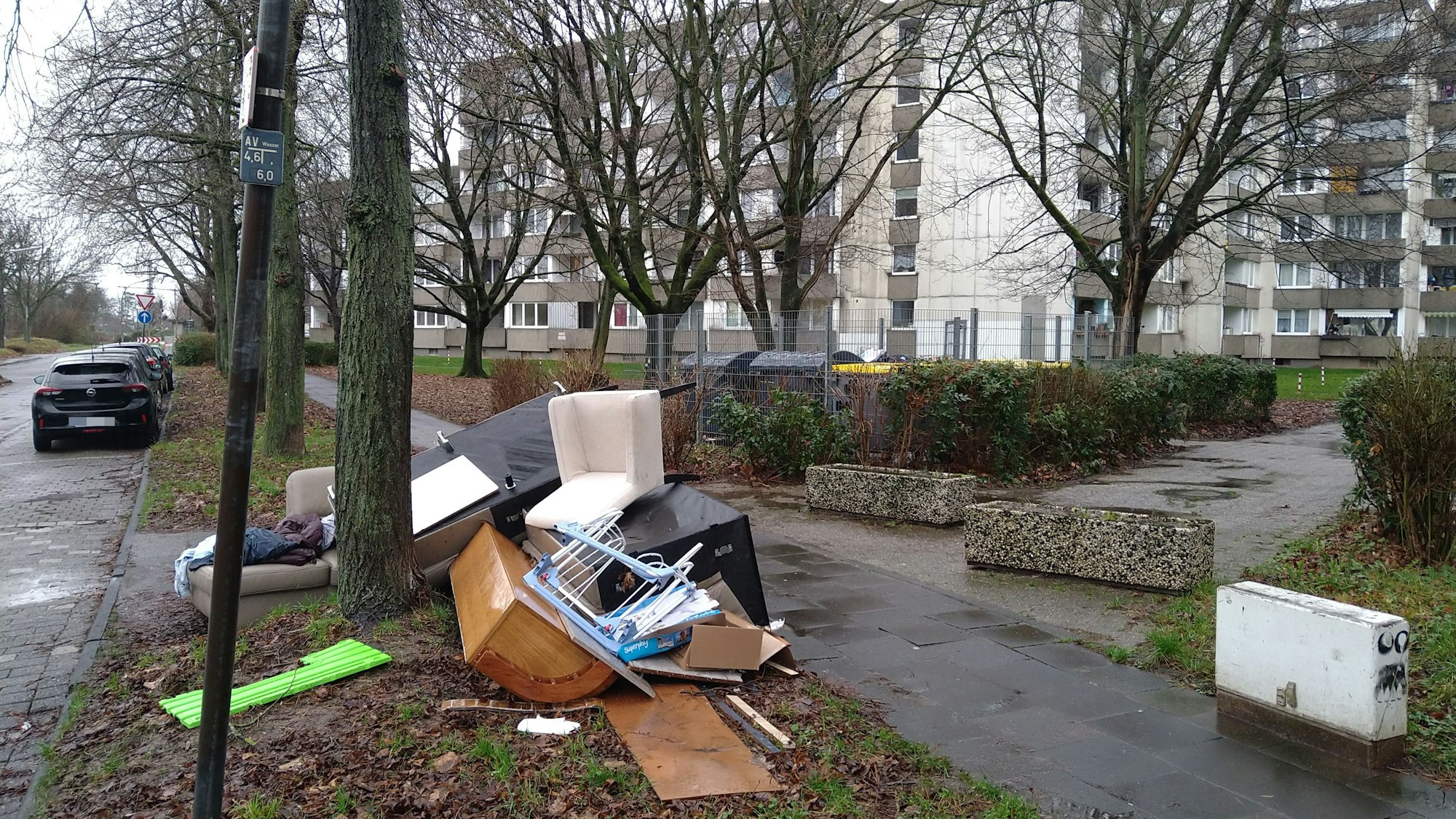 Sperrmüll liegt auf dem Grünstreifen zwischen Straße und Bürgersteig, im Hintergrund sind große Wohnblocks zu sehen.