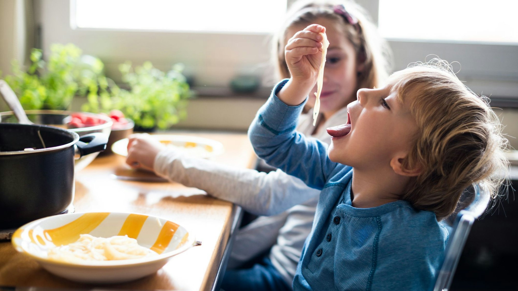 Ein Junge steckt trockene Spaghetti in den Mund.