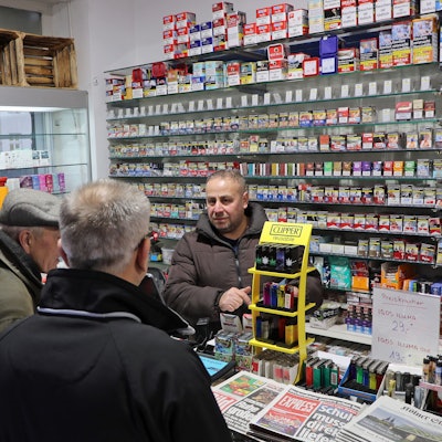 Auf dem Bild ist der Betreiber eines Kiosks mit Kunden zu sehen.