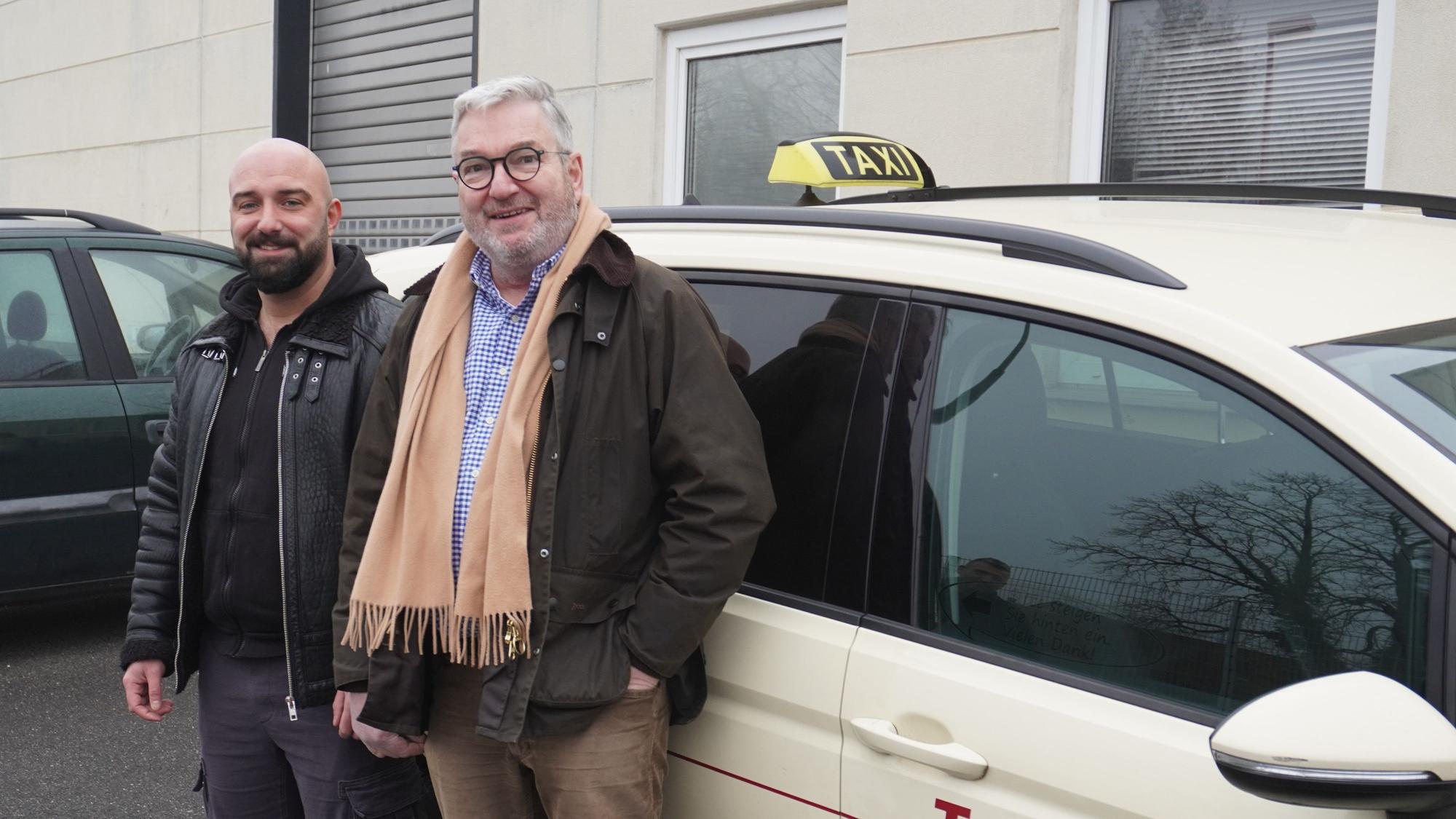 Kerim Kasikci und Thomas Naurath stehen vor einem Taxi.