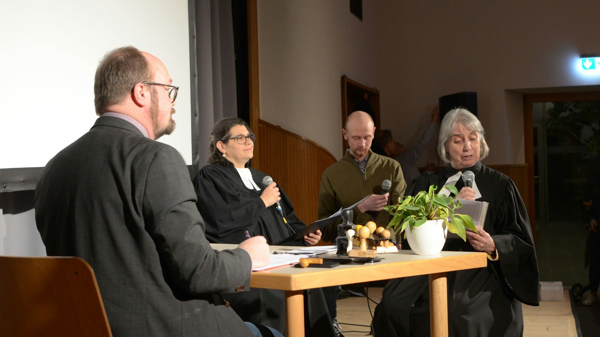 Vier Akteure und Akteurinnen sitzen bei ihrem Sketch auf der Bühne an einem Schreibtisch.