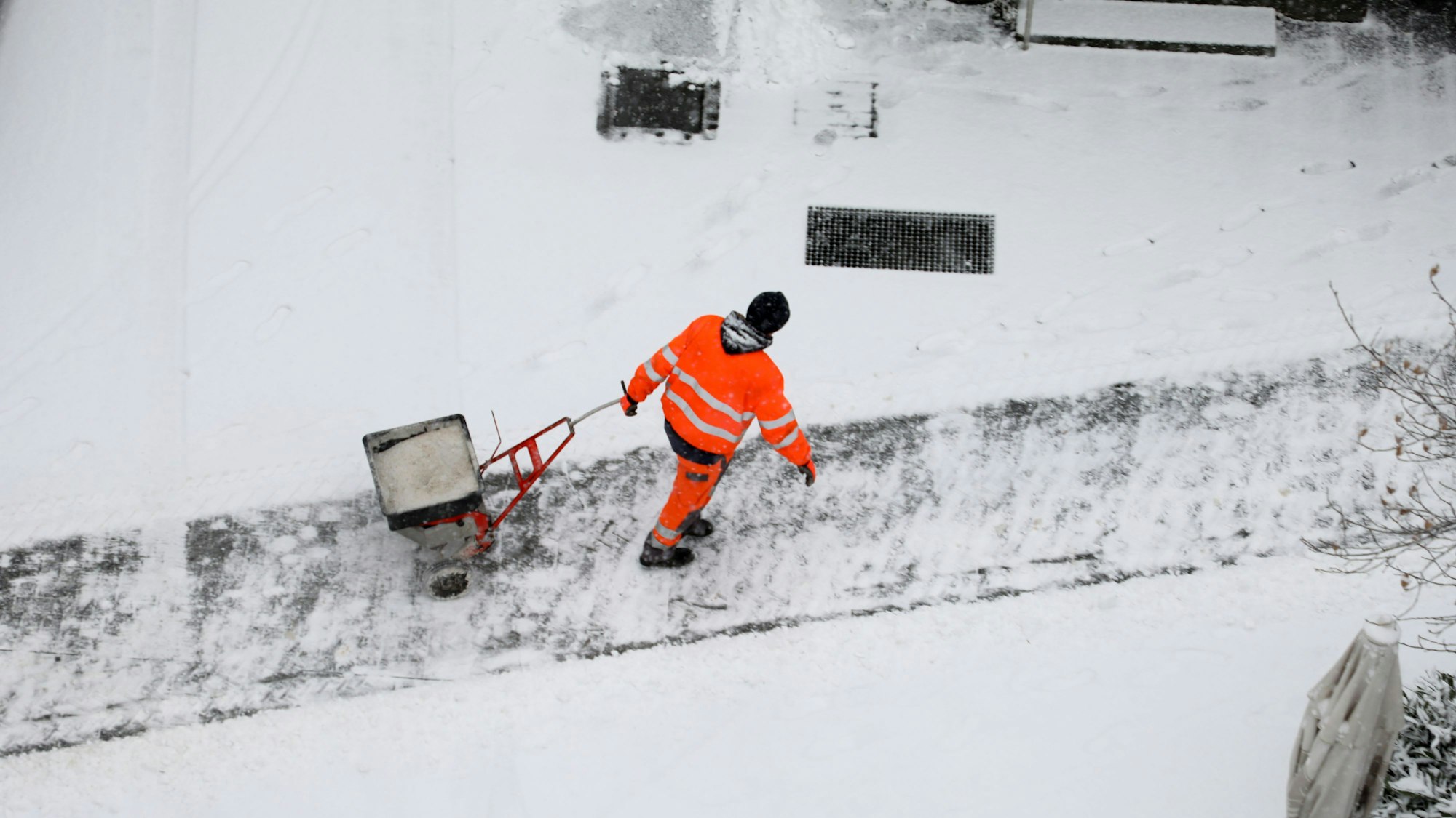 Mann in Arbeitsklamotten streut Sal auf einen zugeschneiten Weg.