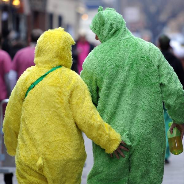 Zwei Menschen in einem gelben und einem grünen Plüsch-Ganzkörperkostüm sind von hinten zu sehen, vor ihnen gehen andere Verkleidete.