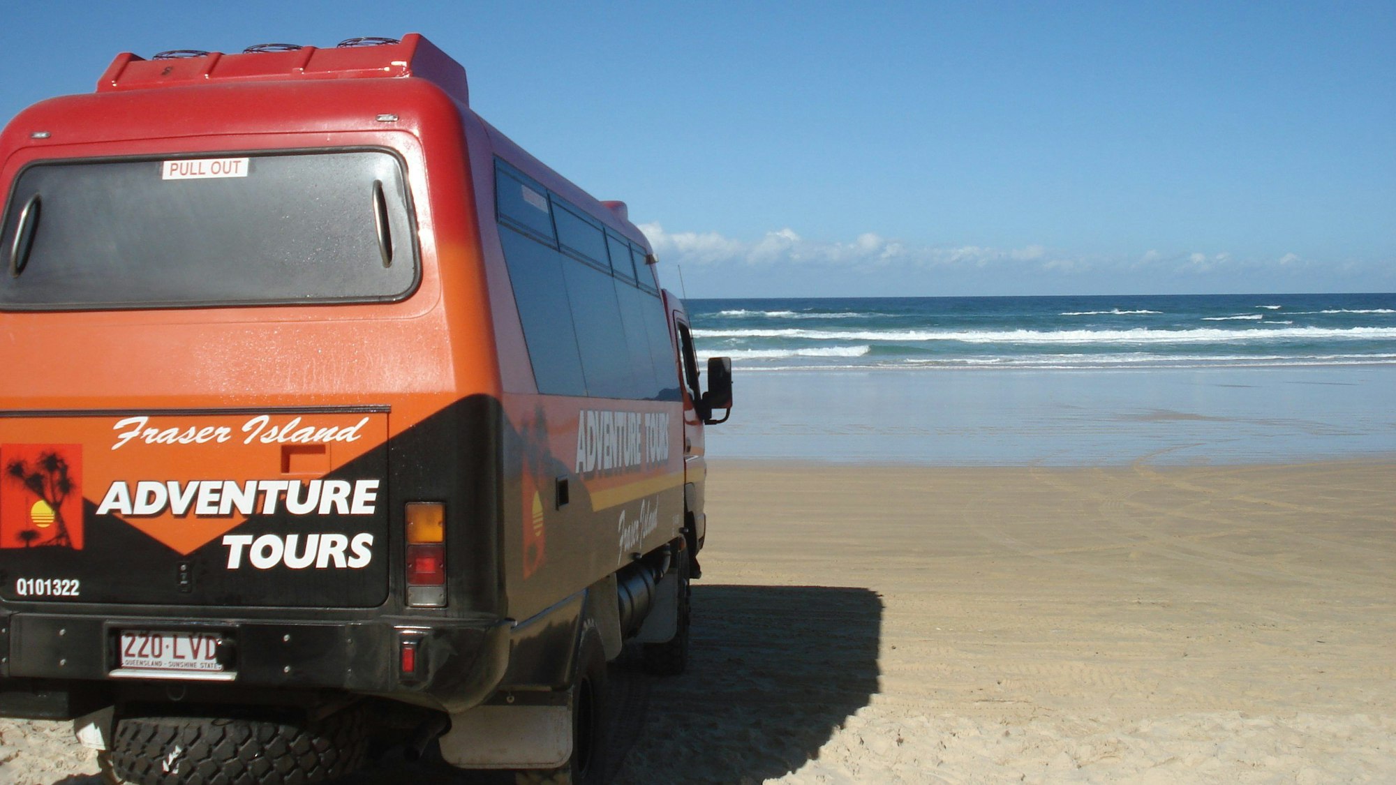 Ein Ausflugs-Truck mit dem Aufdruck Fraser Island steht am Strand.