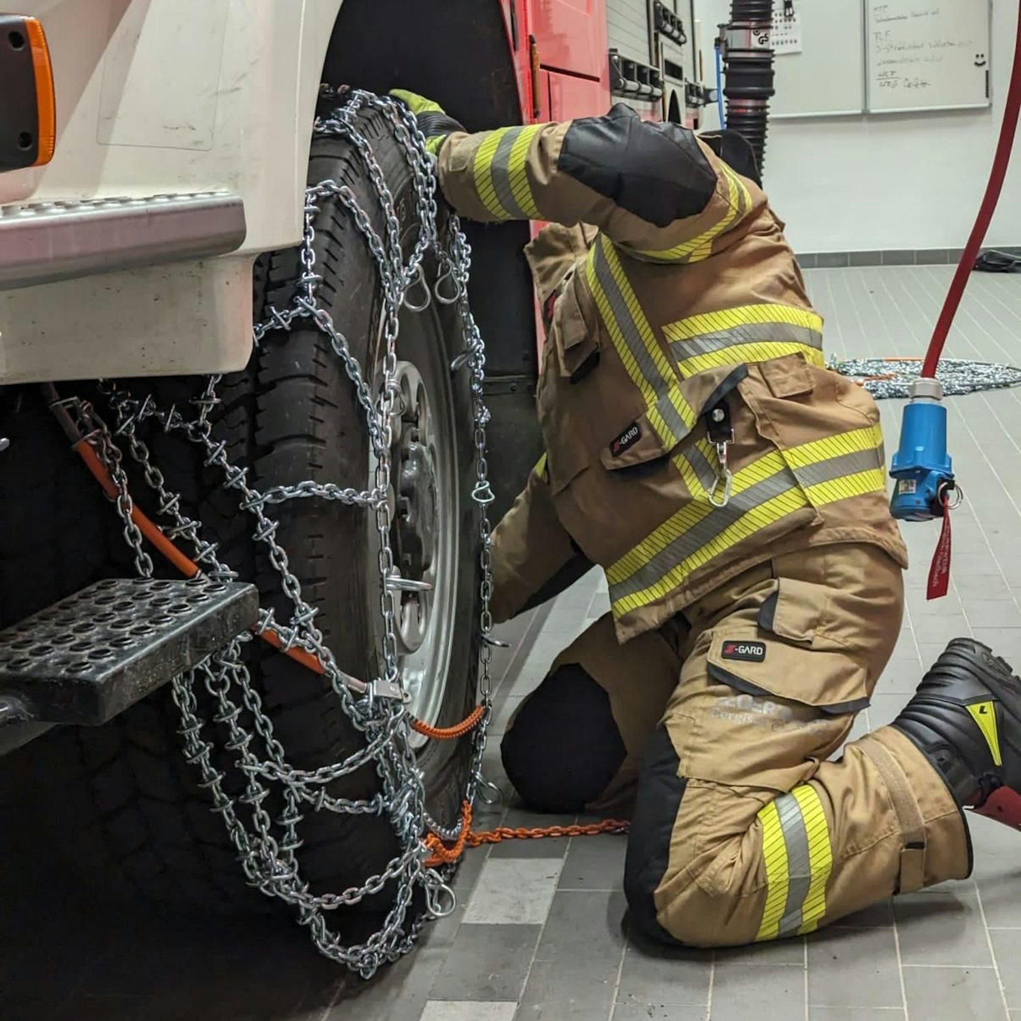 Ein Feuerwehrmann zieht eine Schneekette auf das Rad eines Feuerwehrfahrzeugs auf.