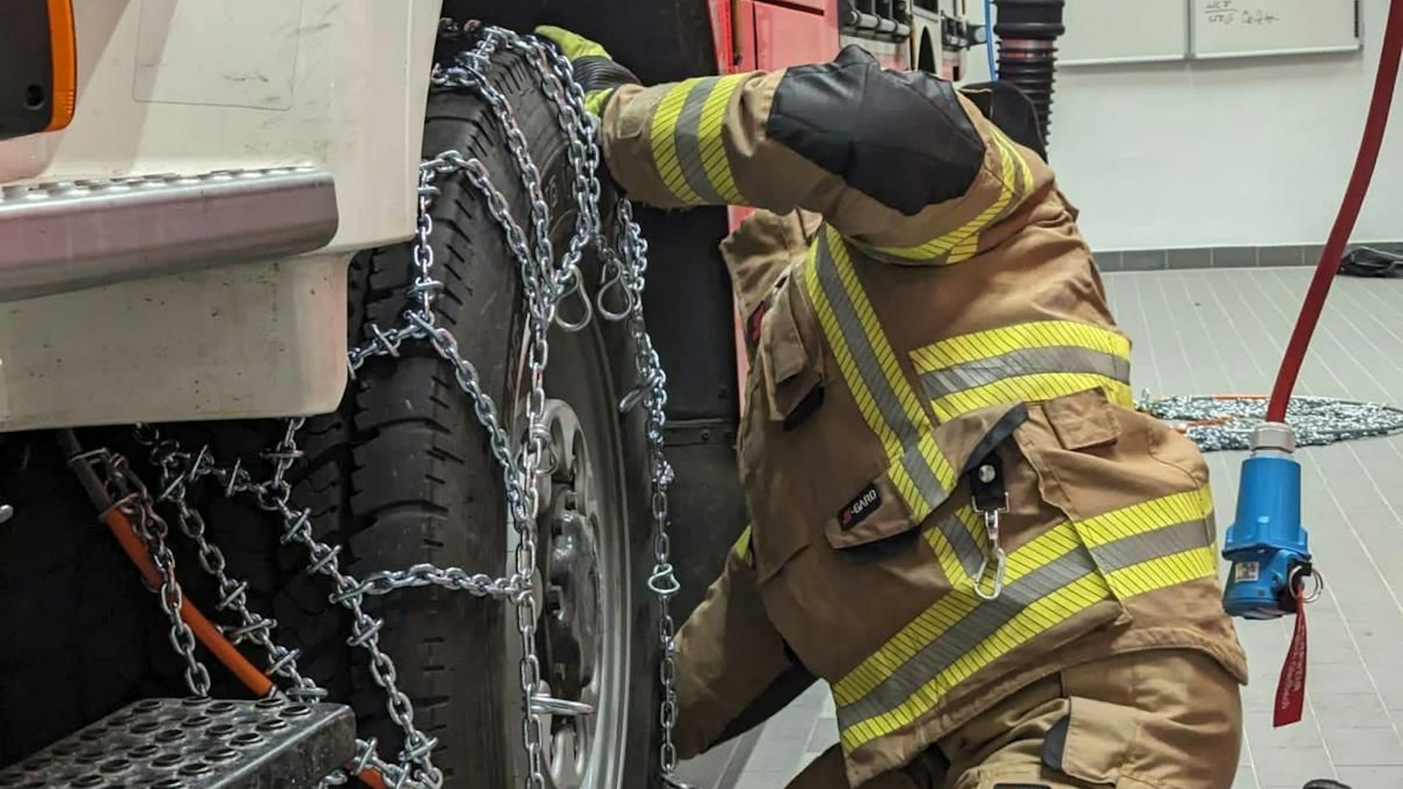 Ein Feuerwehrmann zieht eine Schneekette auf das Rad eines Feuerwehrfahrzeugs auf.
