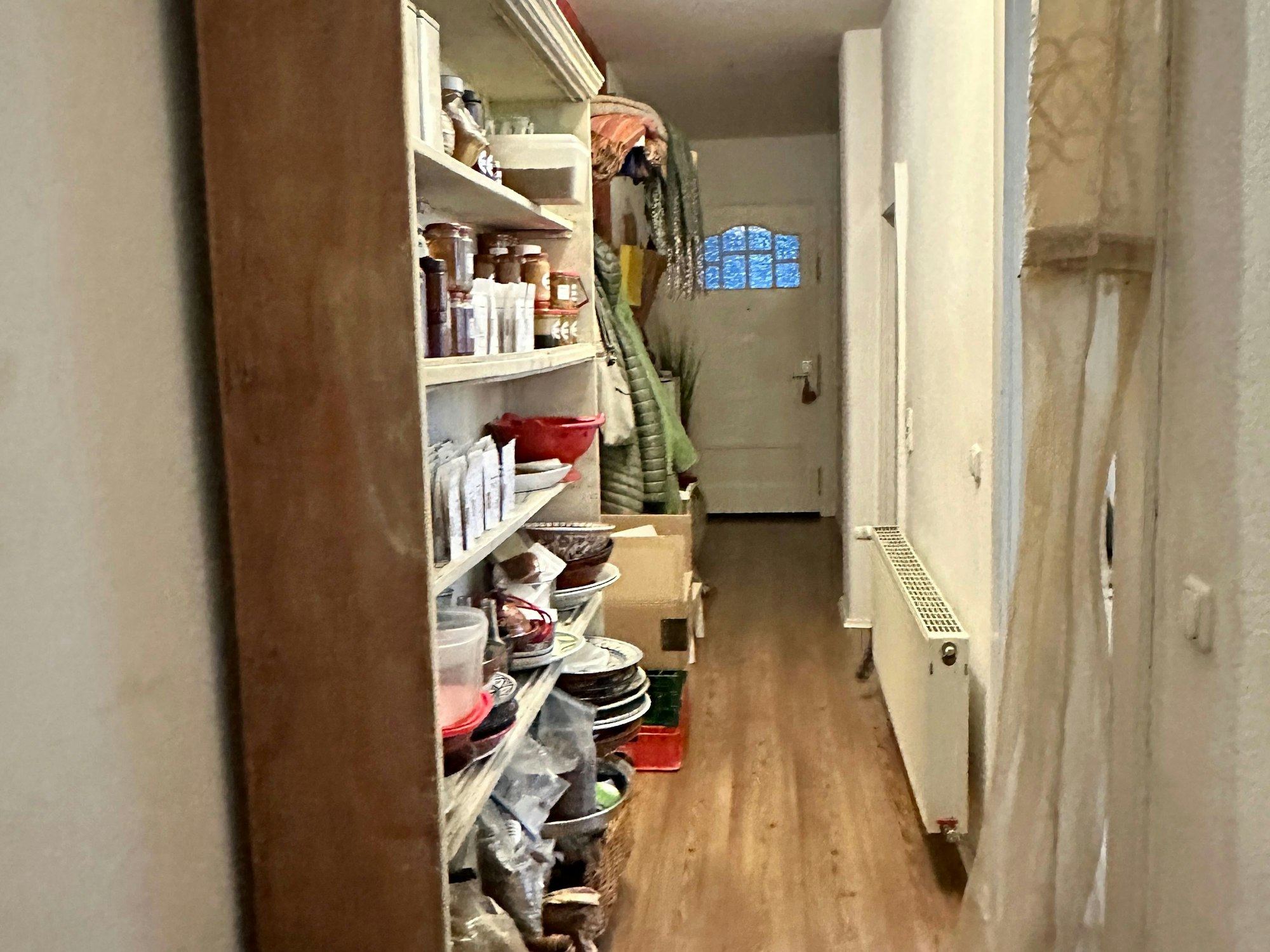 In einem langen Flur stehen ein Regal und eine Garderobe und Kartons.