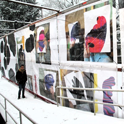 Ein Mann steht an einem riesigen Bauzaun, der mit verschiedenen Bildern dekoriert ist.