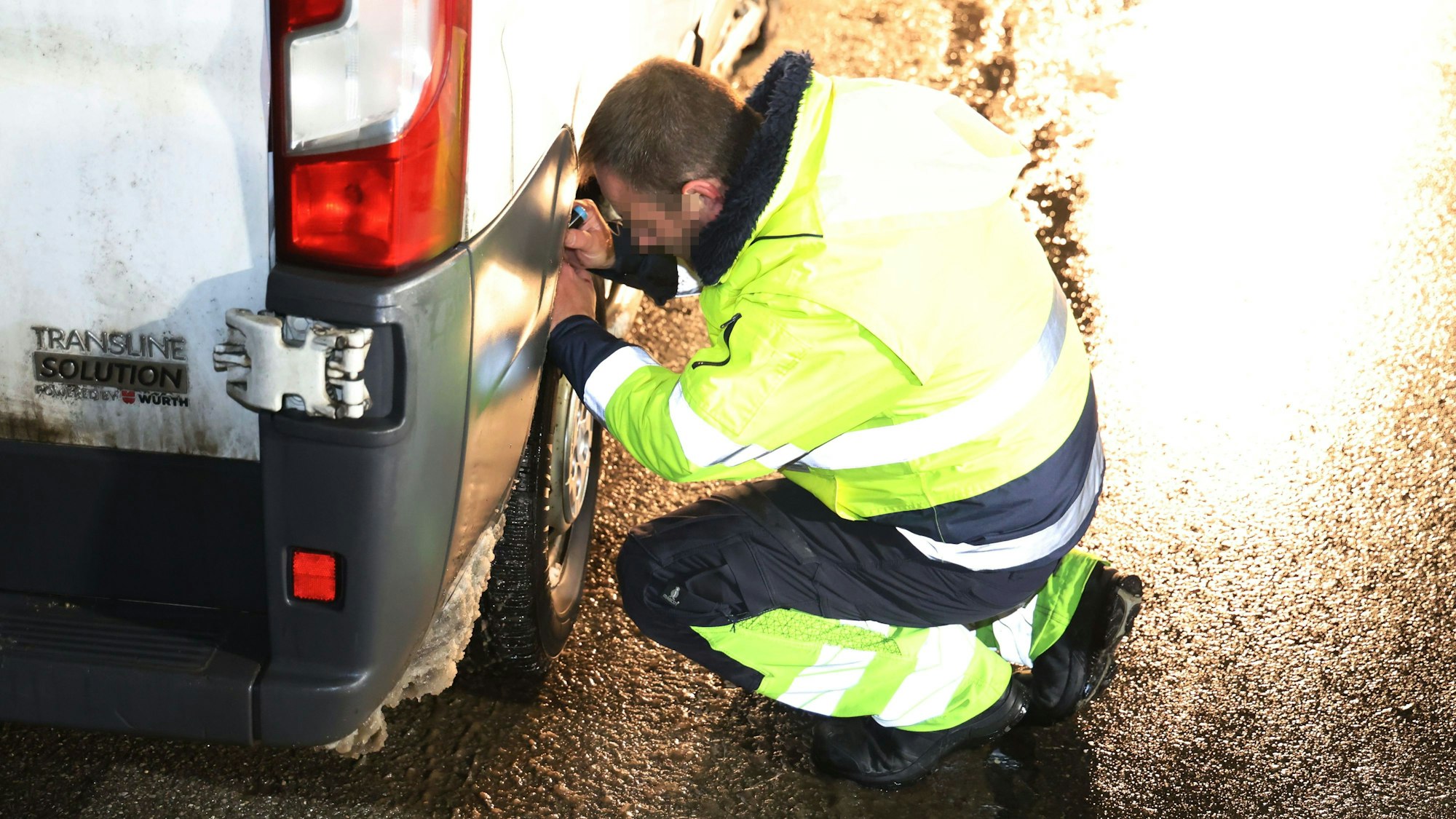 Ein Experte in Warnkleidung untersucht den rechten Hinterreifen eines Sprinters.