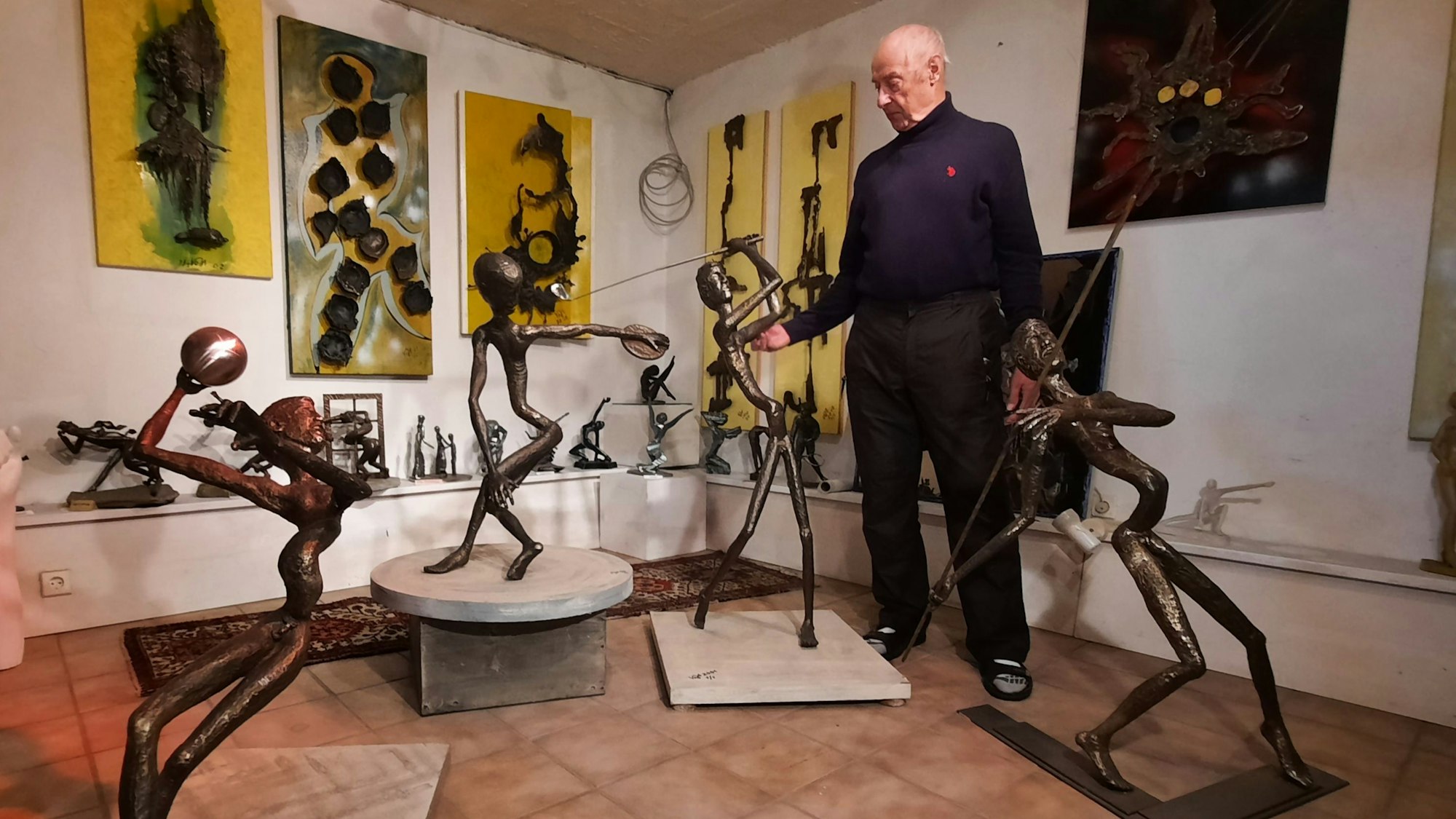 Ein Mann steht neben mehreren feingliedrigen Bronzefiguren.