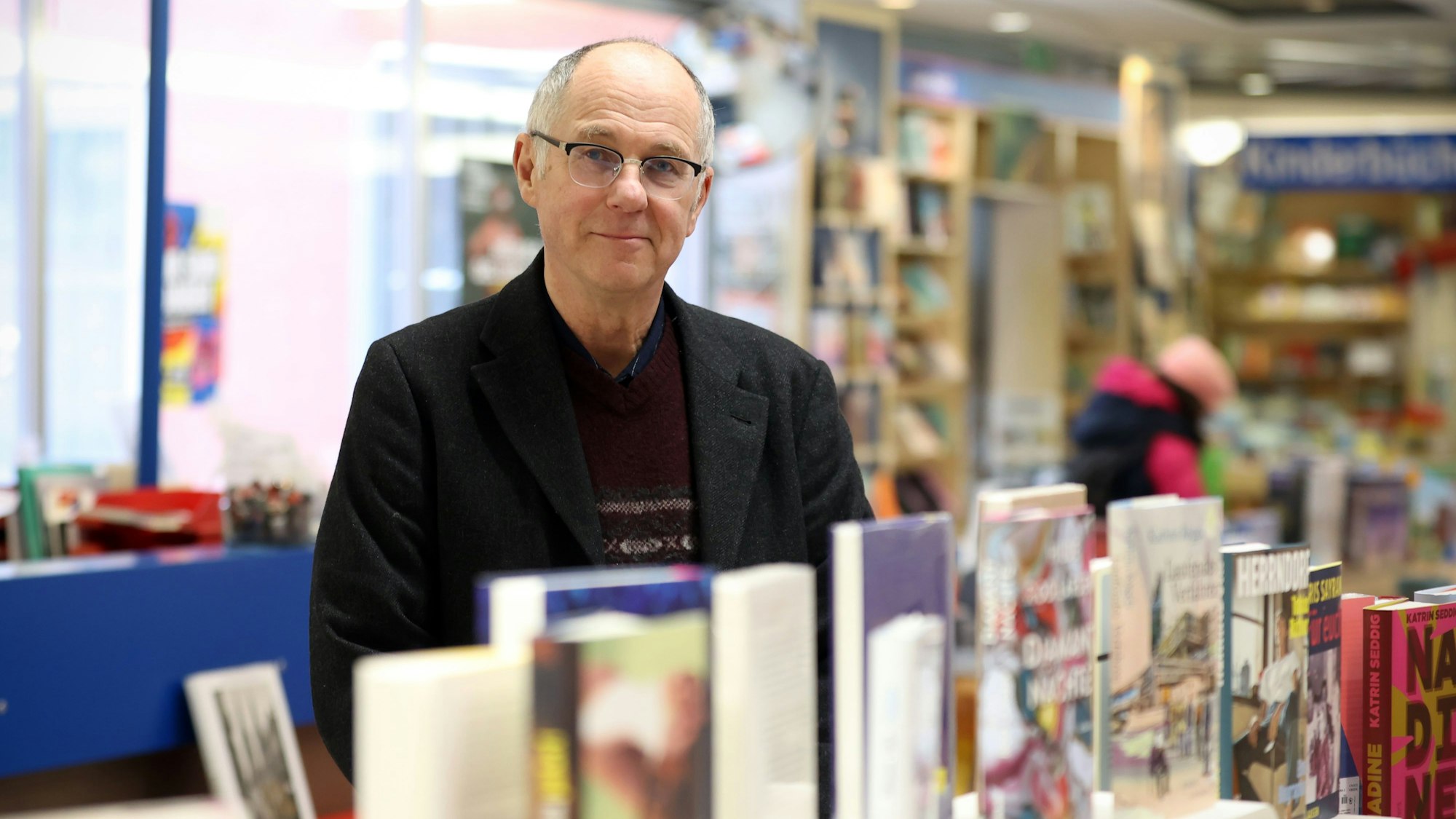 Ein Mann mit Brille steht hinter einem Tisch, auf dem viele Bücher ausgestellt sind.
