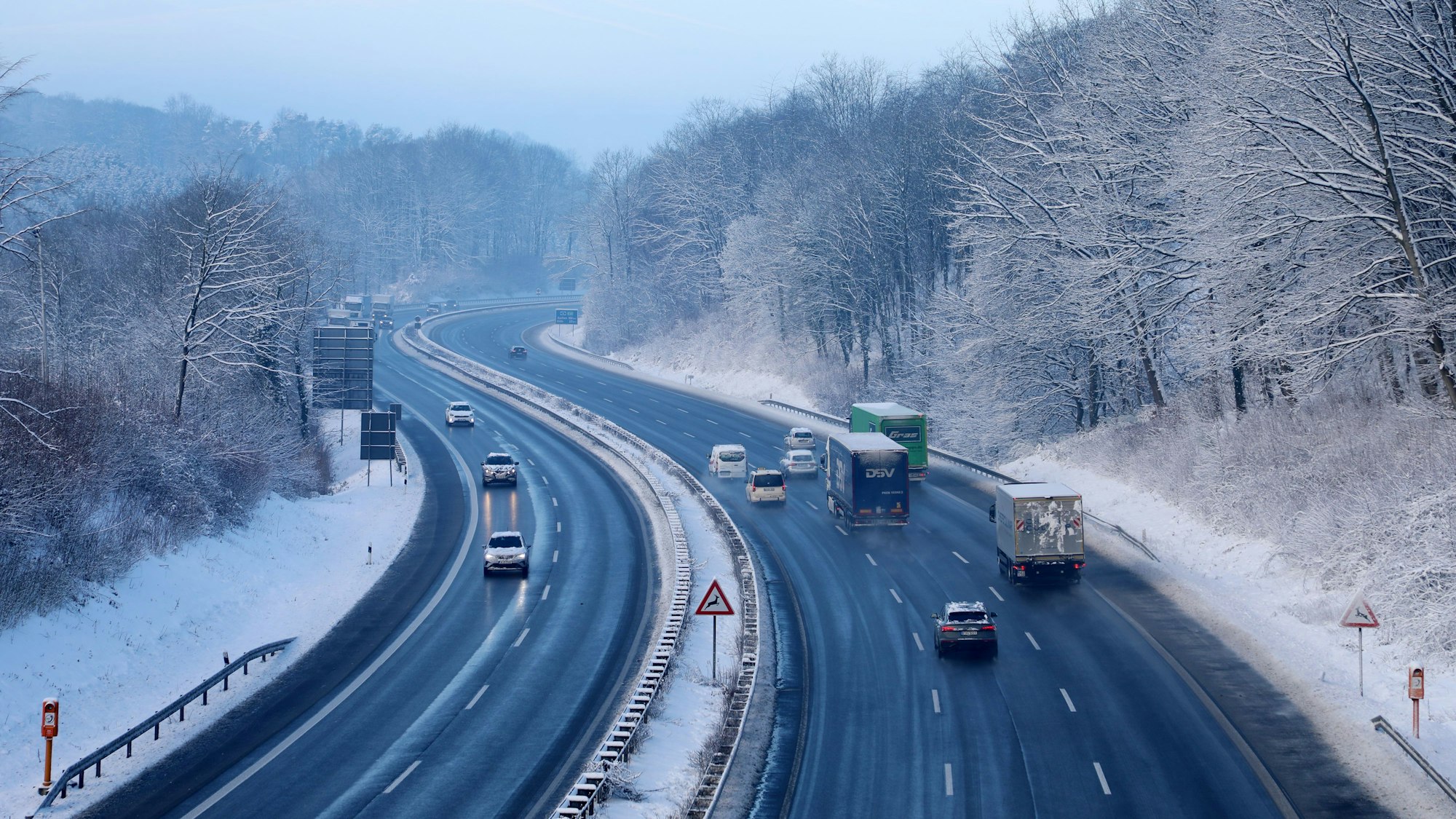 Autos fahren auf der Autobahn 4 durch eine winterliche Landschaft den Berg bei Overath hinauf.