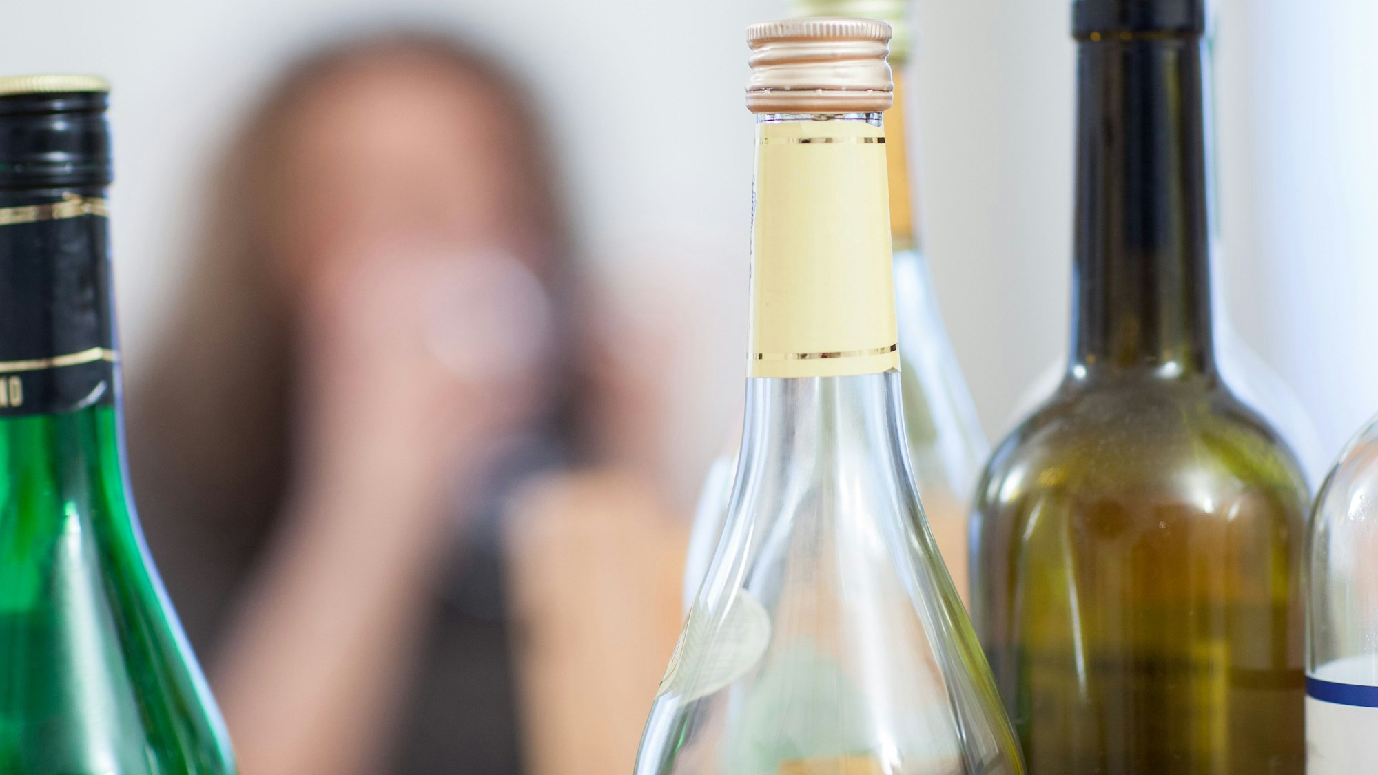 Leere Weinflaschen, im Hintergrund unscharf ein Gesicht.