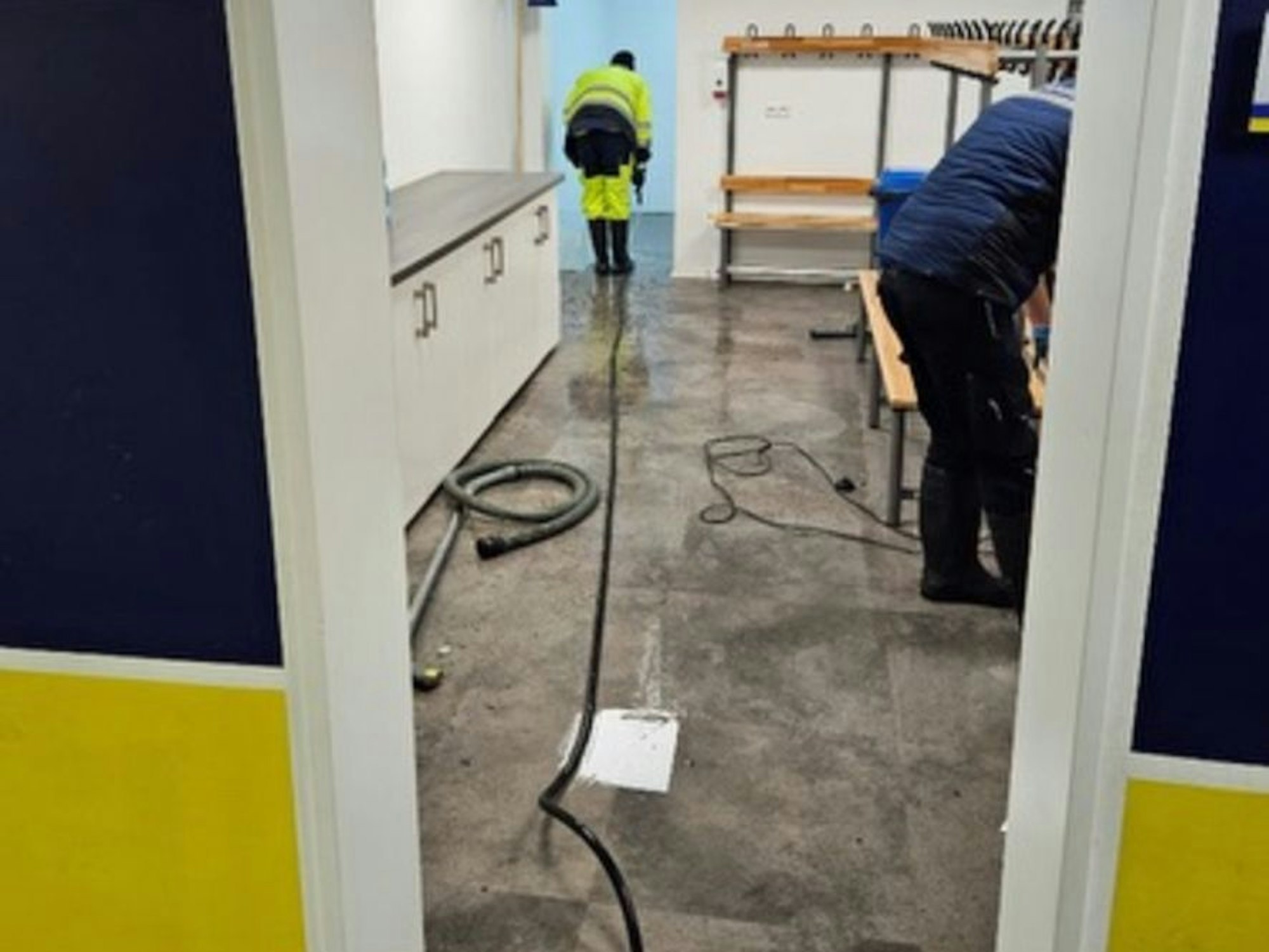 Ein Mann versucht mit einem Gerät Feuchtigkeit aus einer Umkleidekabine zu saugen.