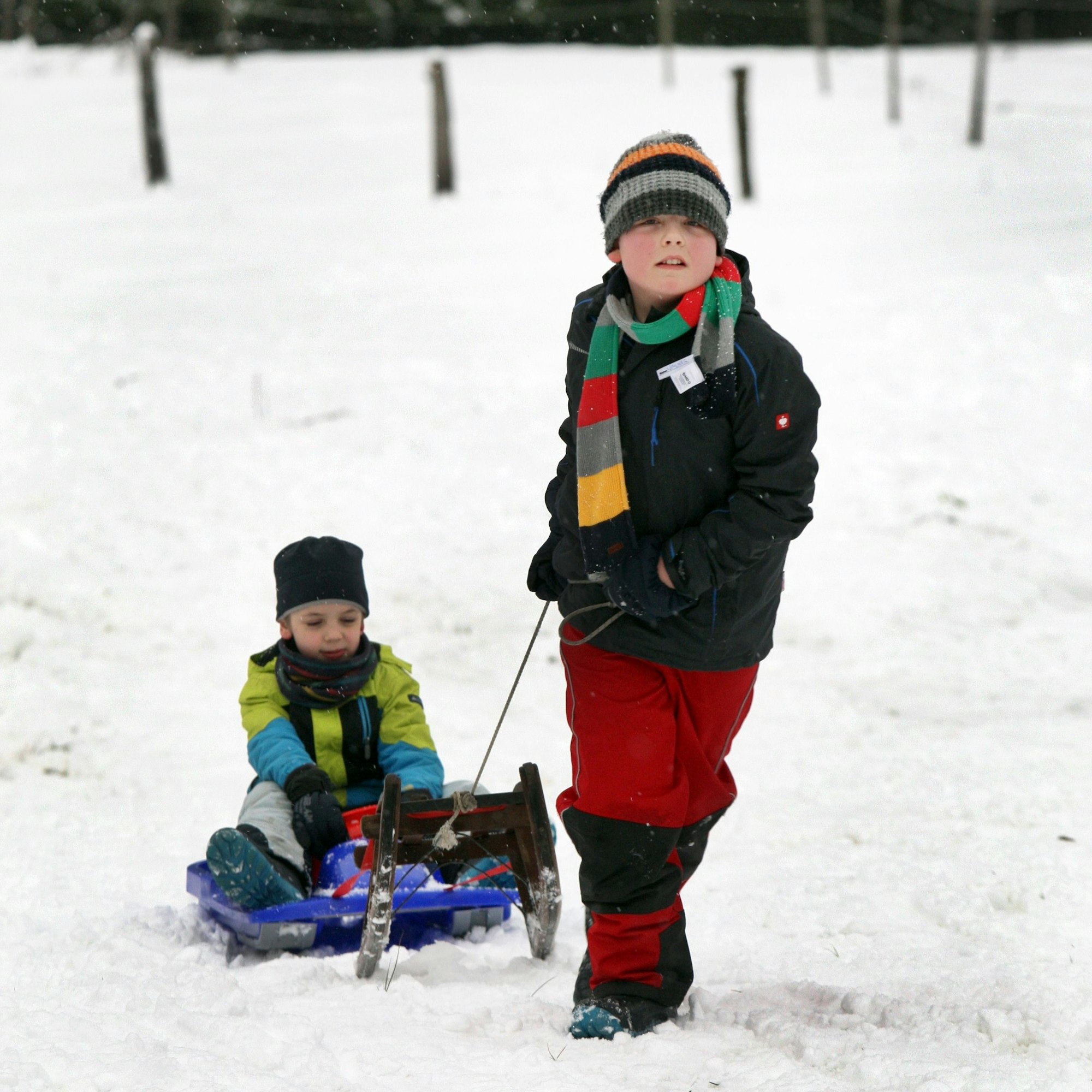 Ein Kind zieht ein anderes auf einem Bob einen Schlittenhang hinauf.