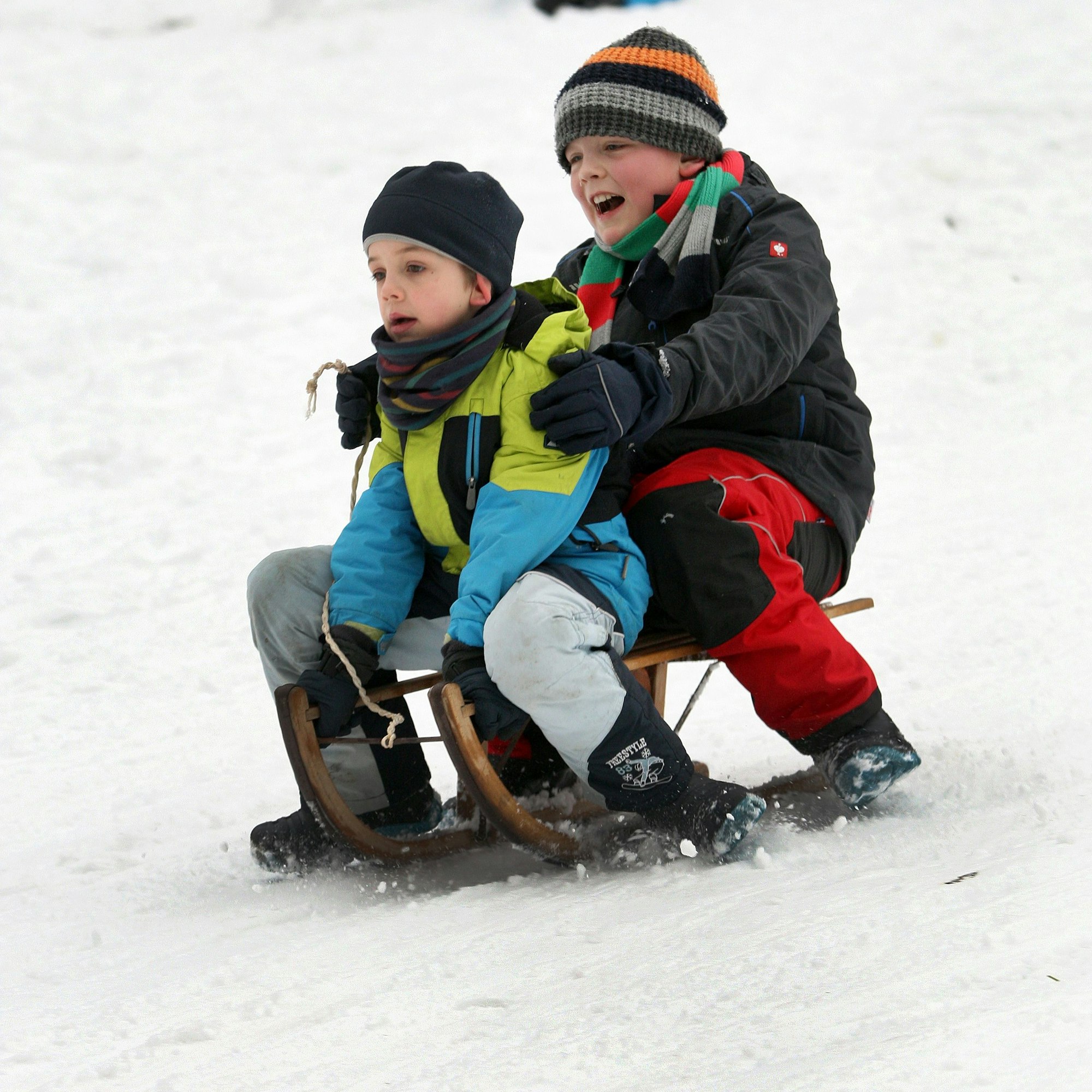 Zwei Kinder fahren auf einem Schlitten einen Abhang hinunter.